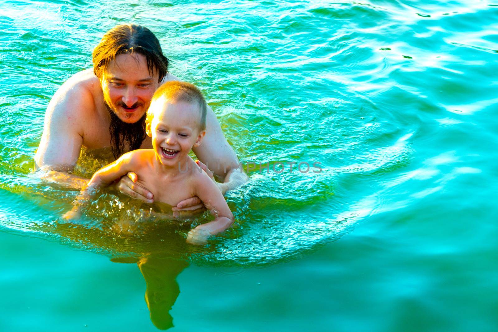 The little boy in his father's arms, in the waves of the sea. Dad with the little child on vacation. by kajasja