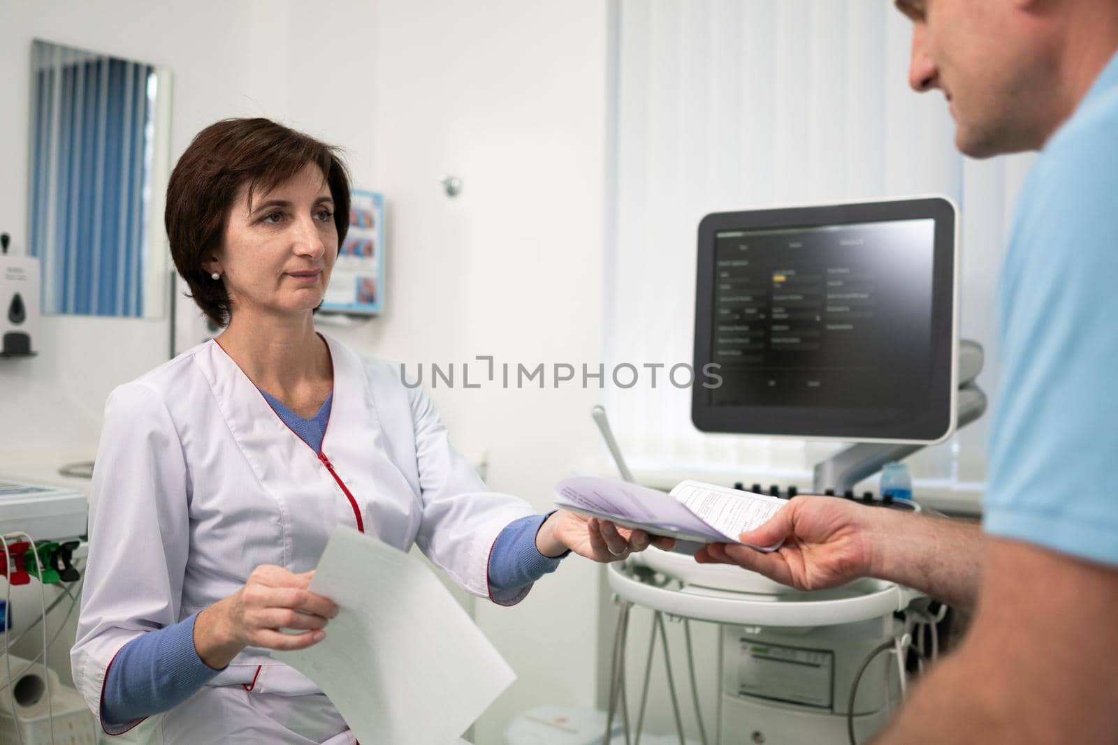 Healthcare and medicine theme. Female general practitioner will see medical tests during health examination of male patient in clinic office. Medical worker in ultrasound diagnostic room with patient by Tomashevska