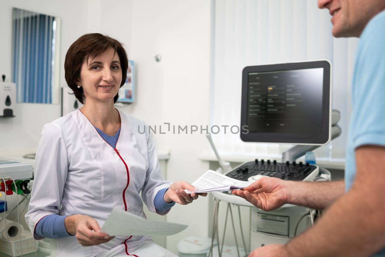 Female doctor consults male patient holding test results in hands in office of clinic. Healtcare and assistance concept. Medical exam. Woman therapist talks to client during consultation at hospital.