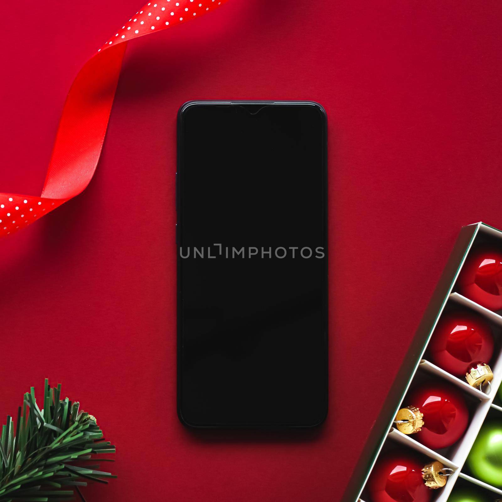 Christmas phone app and holiday message concept. Smartphone with blank black screen and xmas decoration on red background as flat lay mockup design by Anneleven