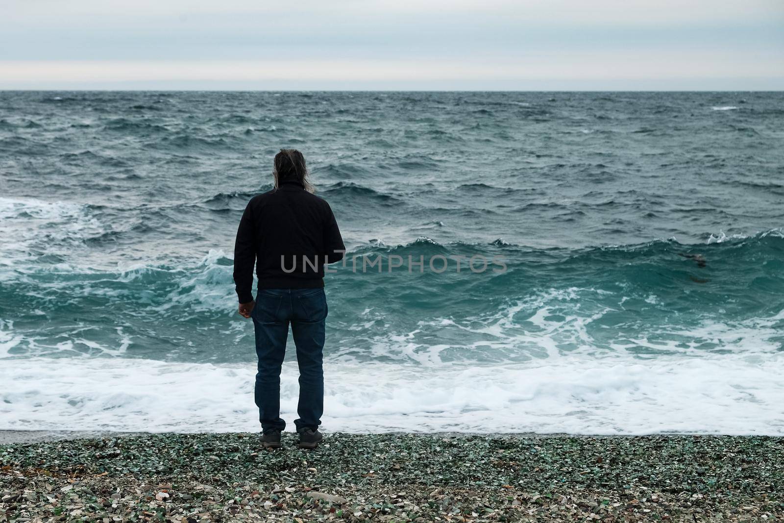 a man stands by the sea on a cloudy day and looks at the big waves.