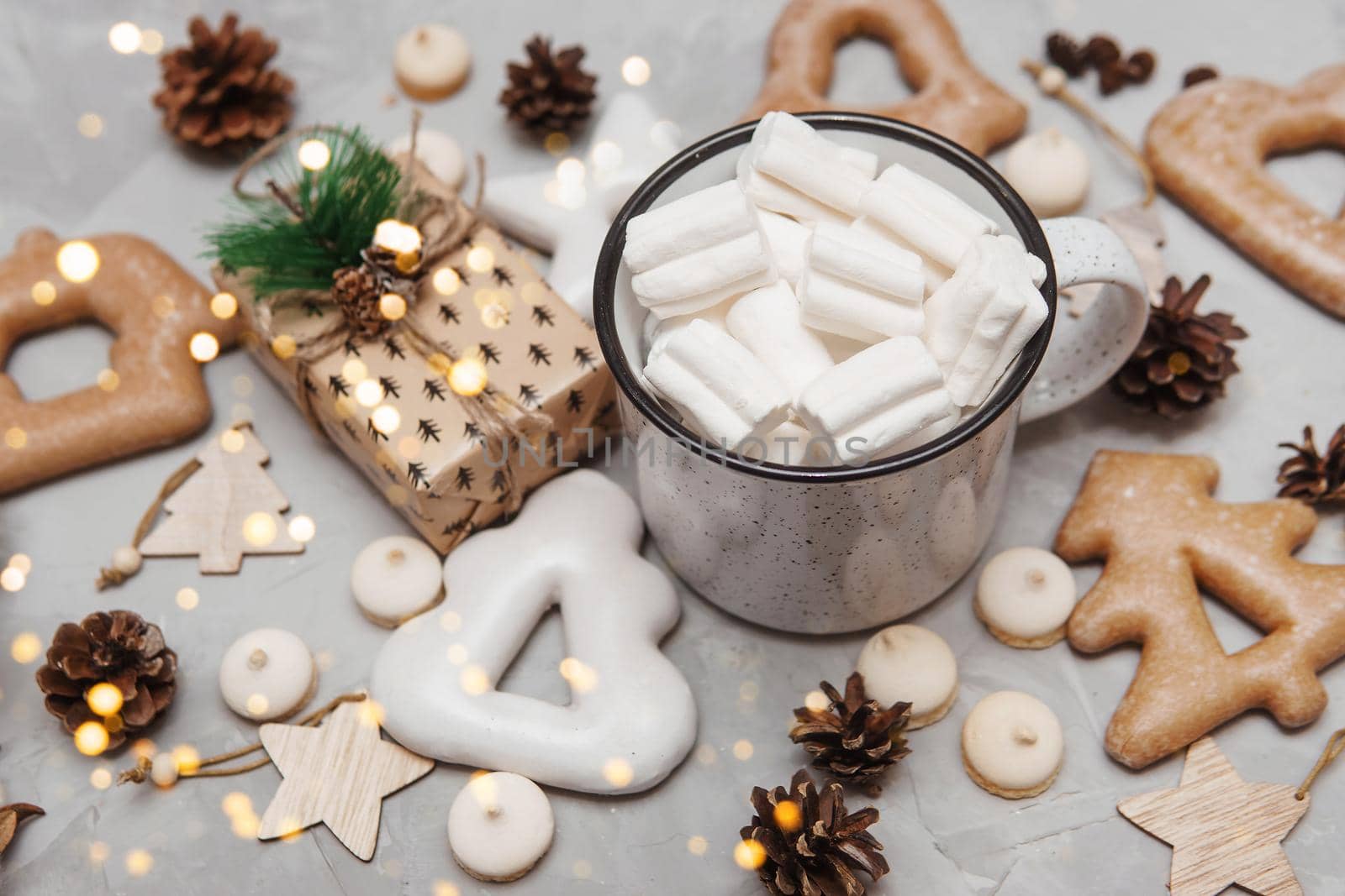 A cup of cocoa with marshmallows and New Year's gingerbread and a gift on the table, bokeh lights in the foreground. The concept of desserts and drinks during the Christmas holidays.
