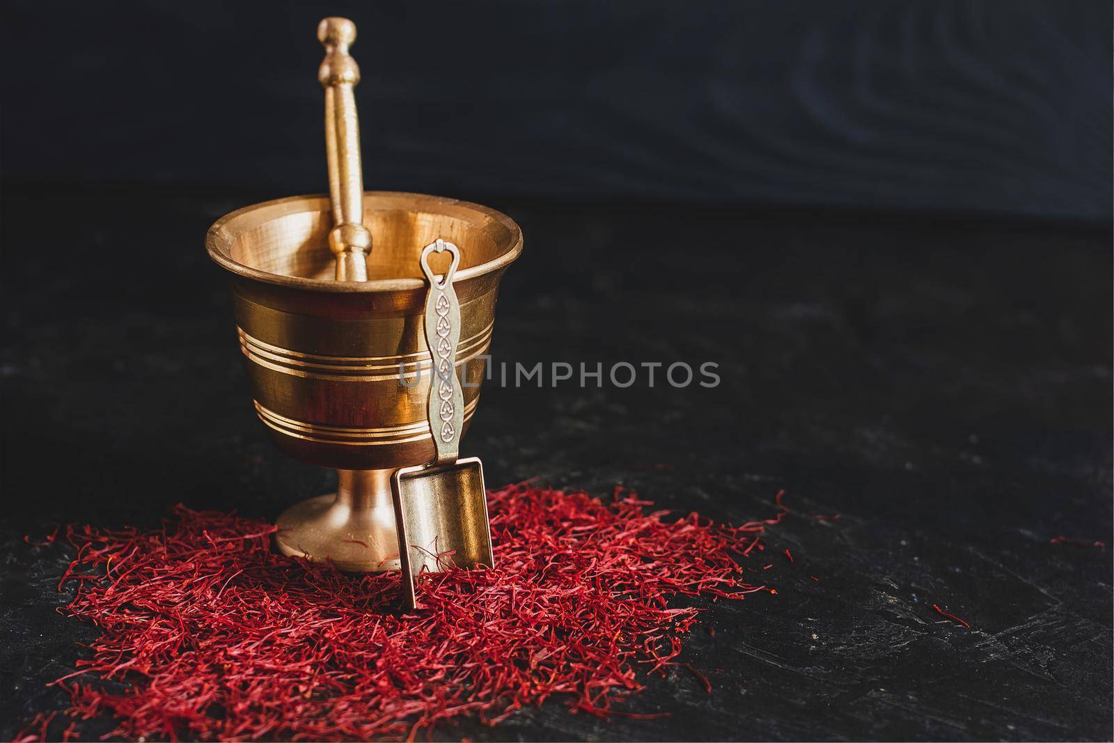 Raw organic red dried saffron spice on wooden background in vintage metal brass mortar with pestle, glass jar and tube by mmp1206