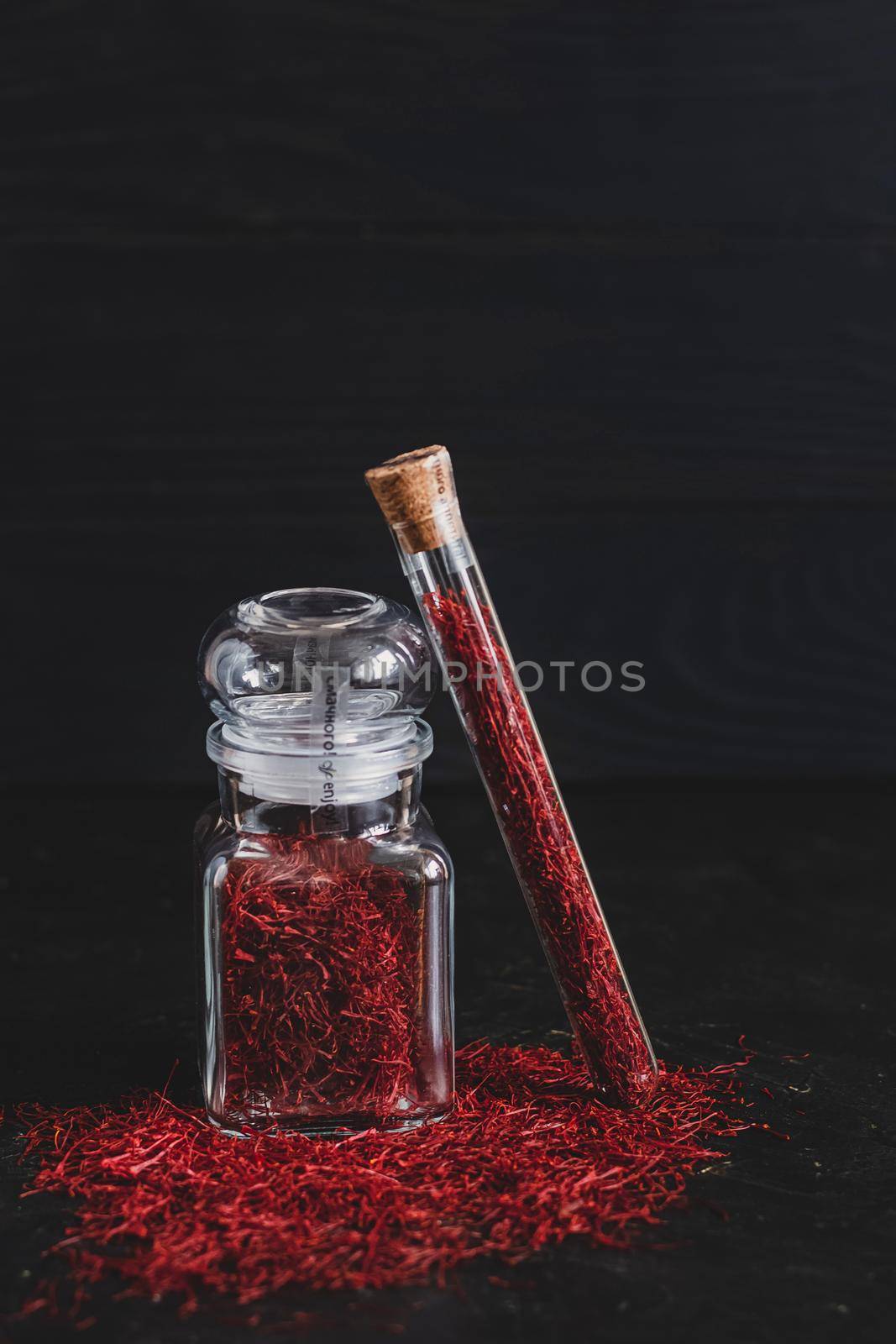 Raw organic red dried saffron spice on wooden background in vintage metal brass mortar with pestle, glass jar and tube.