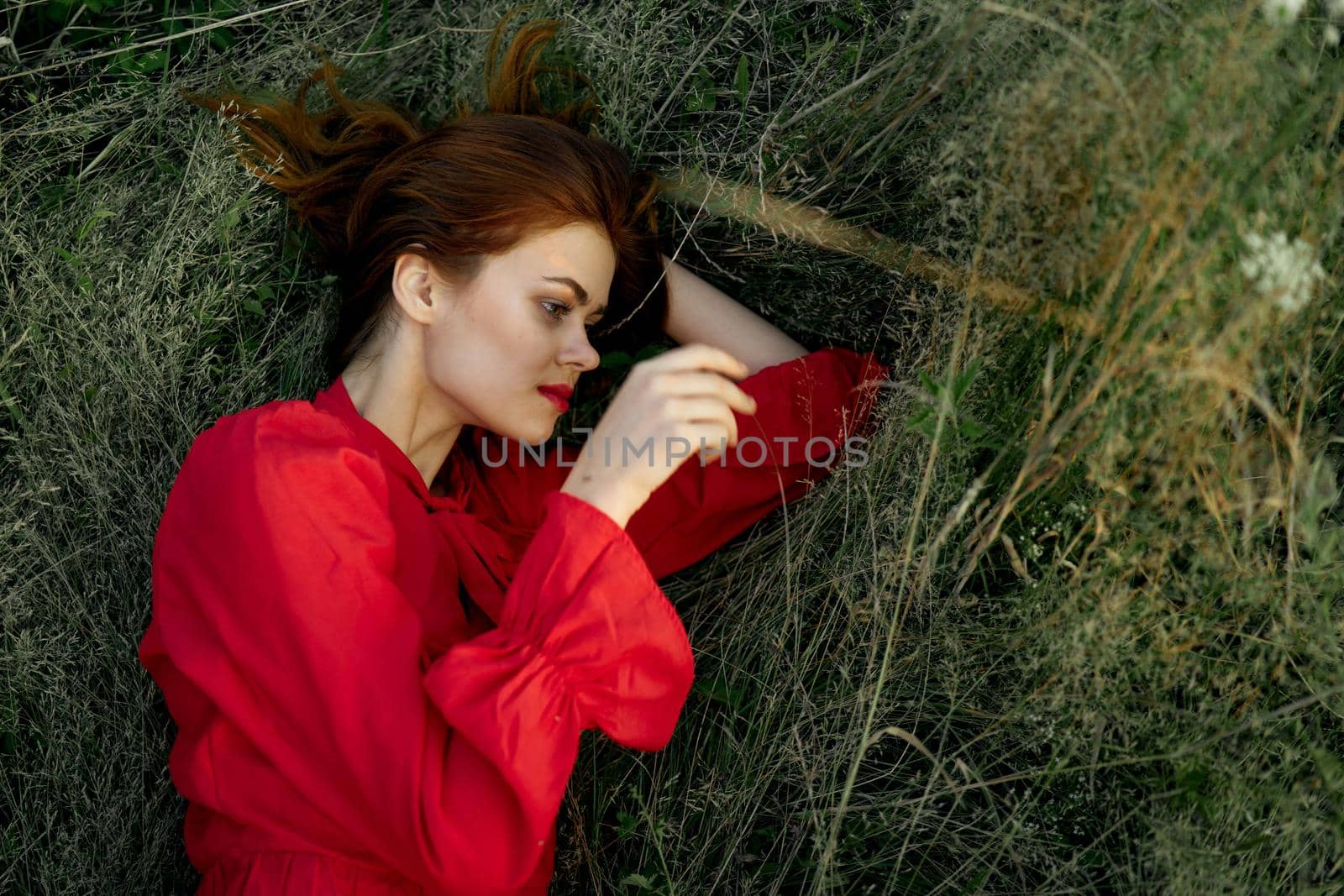 pretty woman in red dress lies on the grass sun summer nature. High quality photo