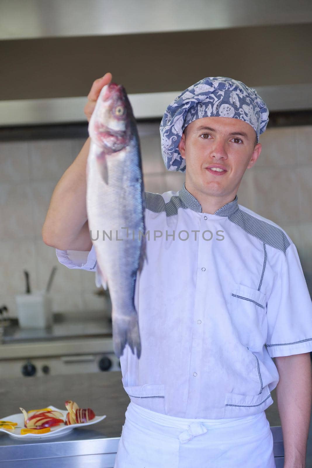 Handsome chef dressed in white uniform decorating pasta salad and seafood fish in modern kitchen