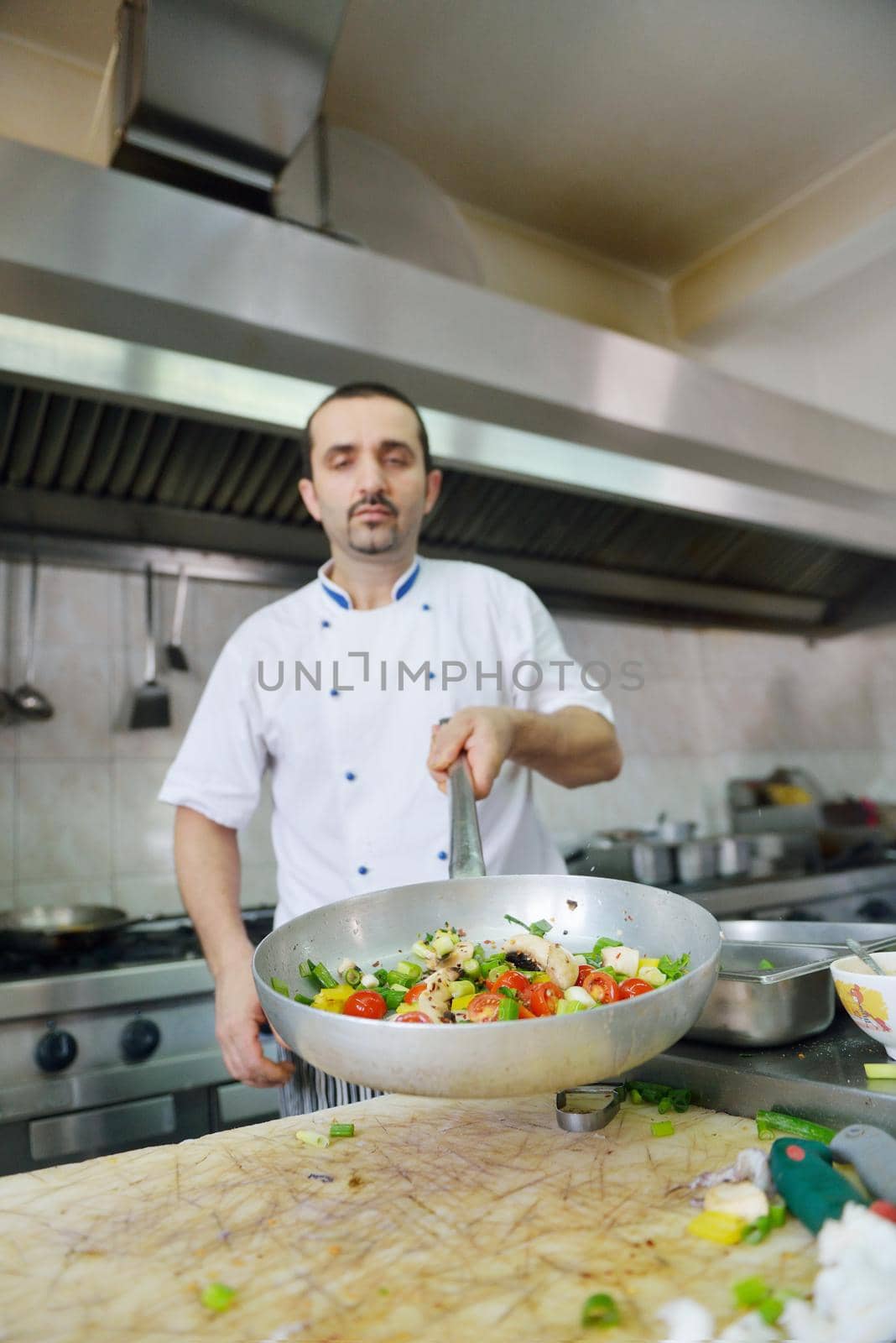 Handsome chef dressed in white uniform decorating pasta salad and seafood fish in modern kitchen