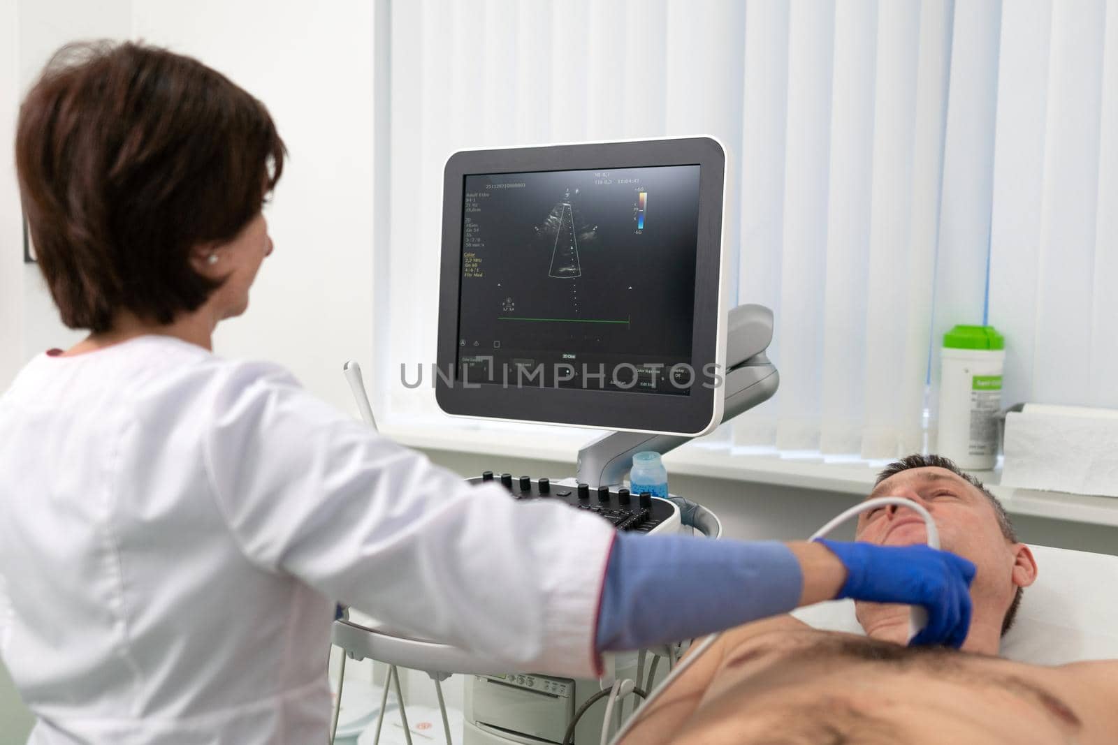 Woman doctor makes heart check of patient man using modern equipment in a cardiology clinic. Female cardiologist is screaning patient heart with ultrasonography, looking at screen. Healthcare concept.