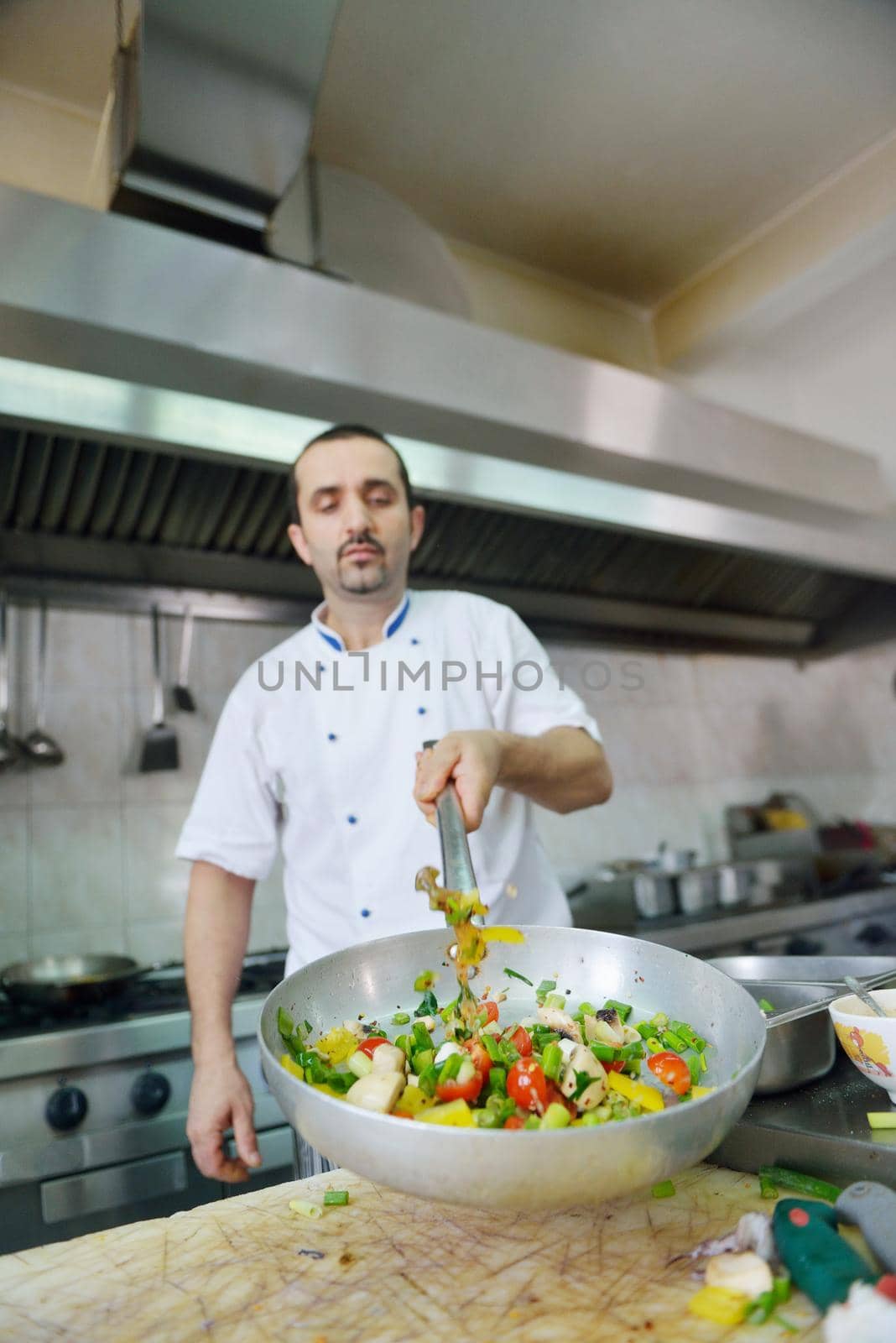 Handsome chef dressed in white uniform decorating pasta salad and seafood fish in modern kitchen