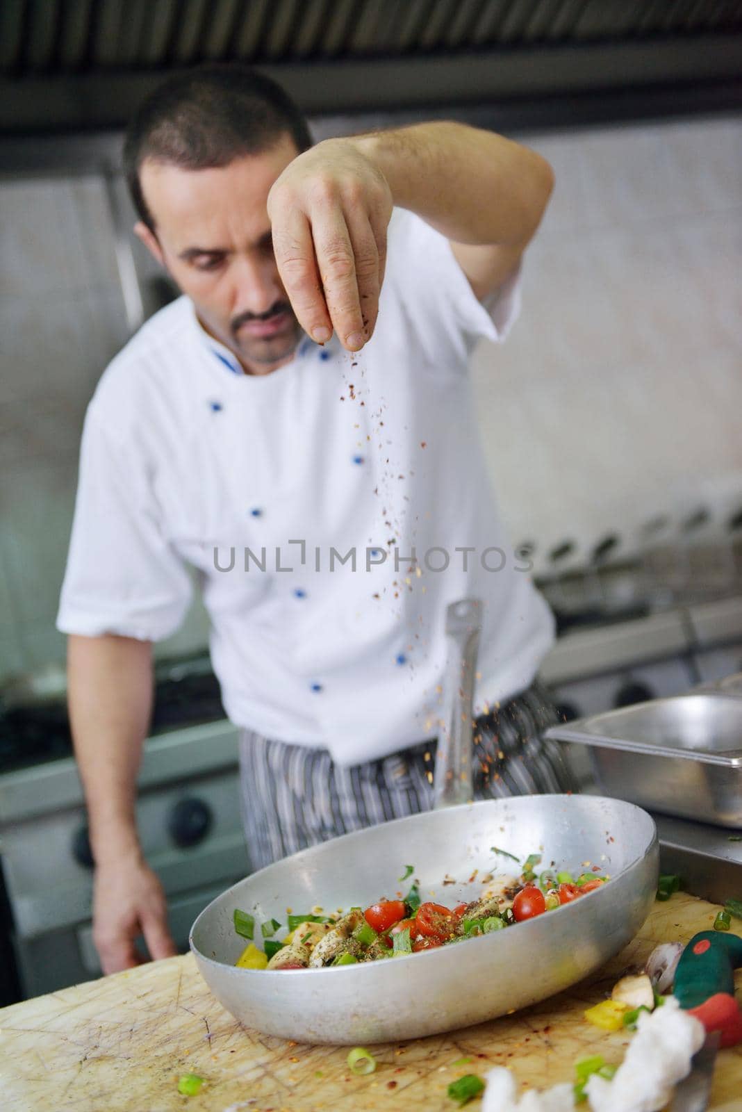 Handsome chef dressed in white uniform decorating pasta salad and seafood fish in modern kitchen