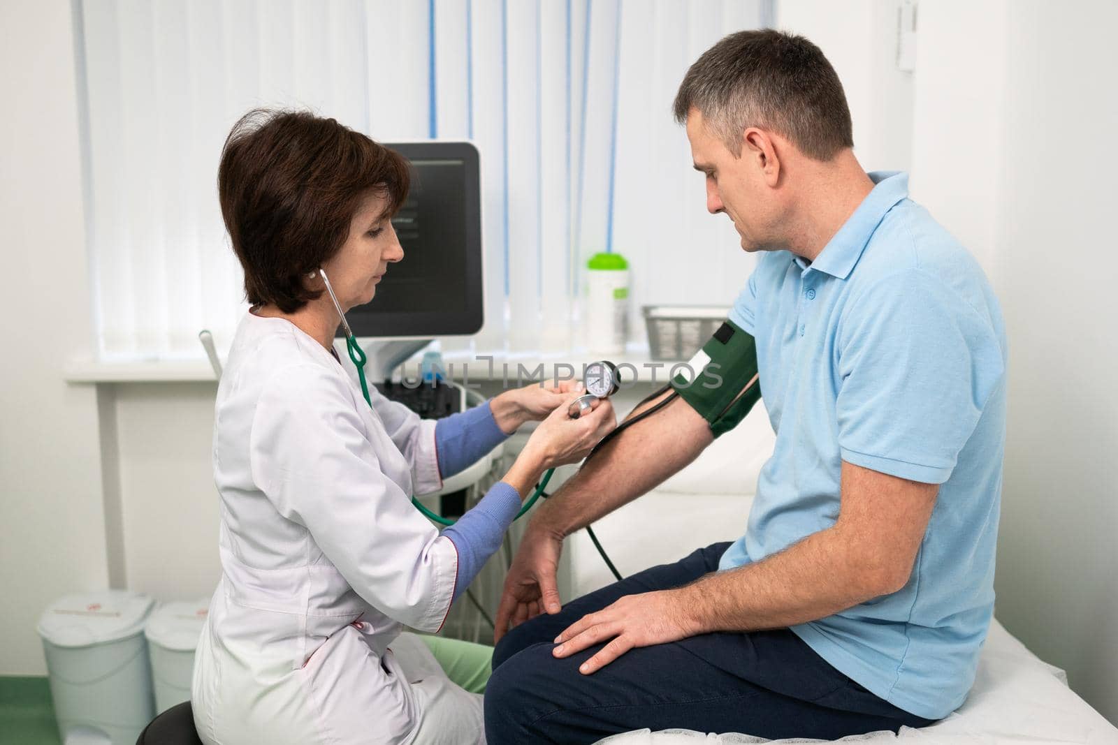 Medical and healthcare concept. Hypertension, high blood pressure and stroke precursors in middle age in men. Medical checkup. Female doctor in general practice measures pressure to patient in clinic by Tomashevska