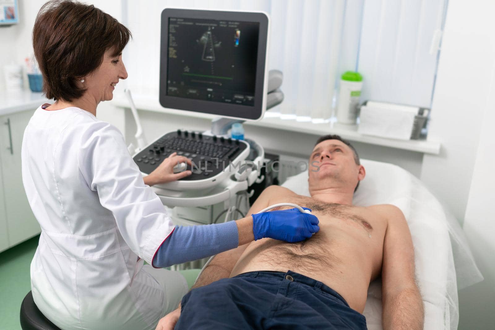 Woman doctor makes heart check of patient man using modern equipment in a cardiology clinic. Female cardiologist is screaning patient heart with ultrasonography, looking at screen. Healthcare concept by Tomashevska