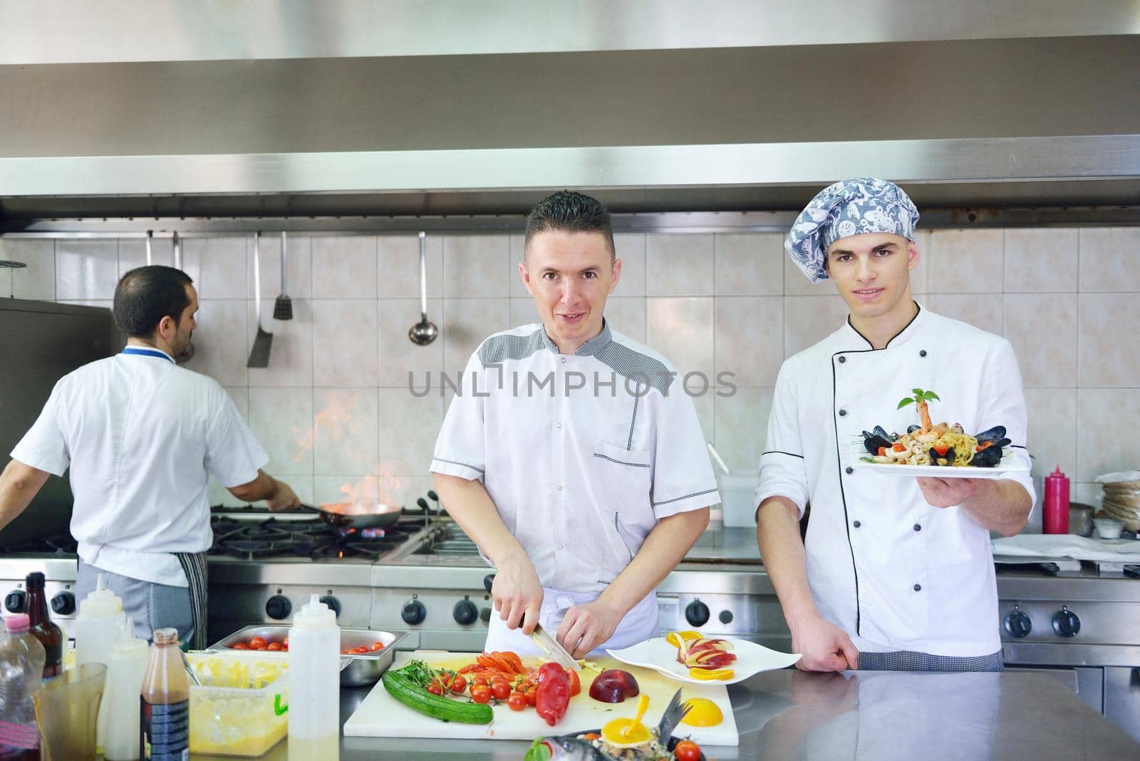 Handsome chef dressed in white uniform decorating pasta salad and seafood fish in modern kitchen