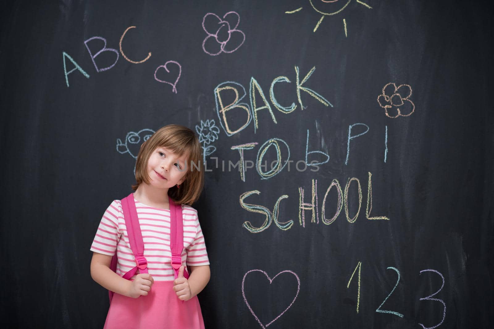 Happy school girl child with backpack writing  back to school on black chalkboard