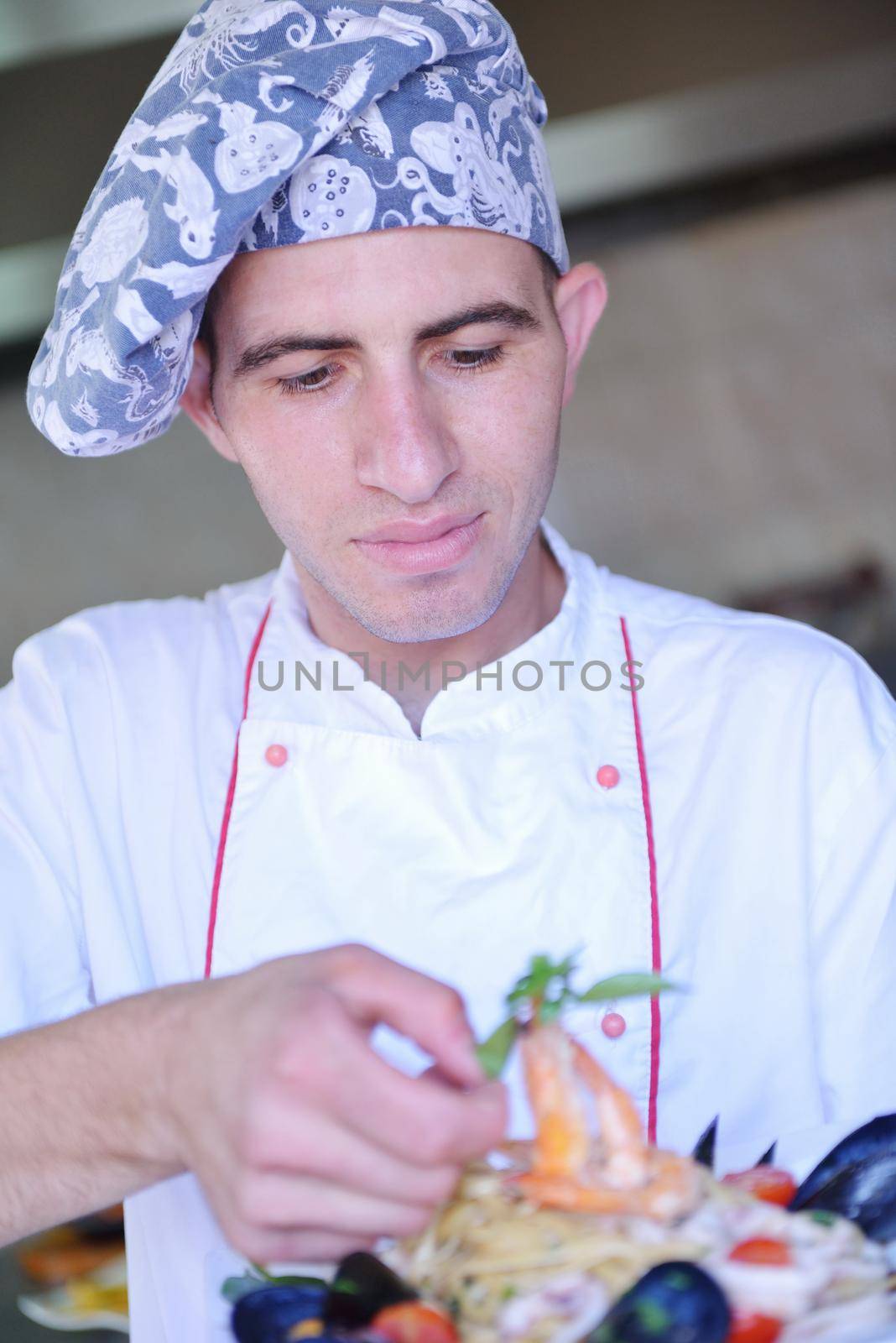 Handsome chef dressed in white uniform decorating pasta salad and seafood fish in modern kitchen