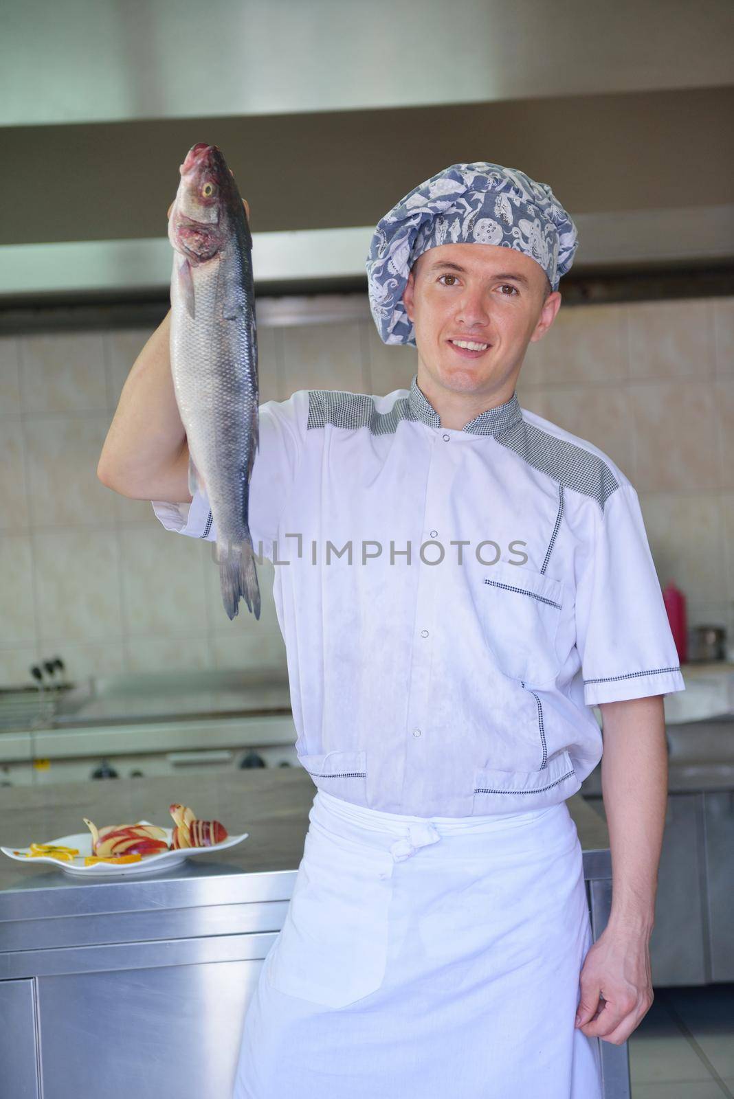 Handsome chef dressed in white uniform decorating pasta salad and seafood fish in modern kitchen