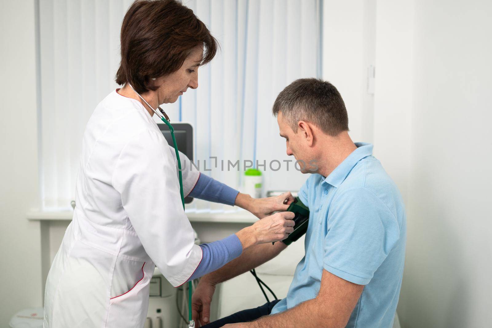 Female doctor measures blood pressure with a sphygmomanometer to male patient at medical examination in clinic office. Cardiologist checks blood pressure of male patient at cardiology hospital by Tomashevska