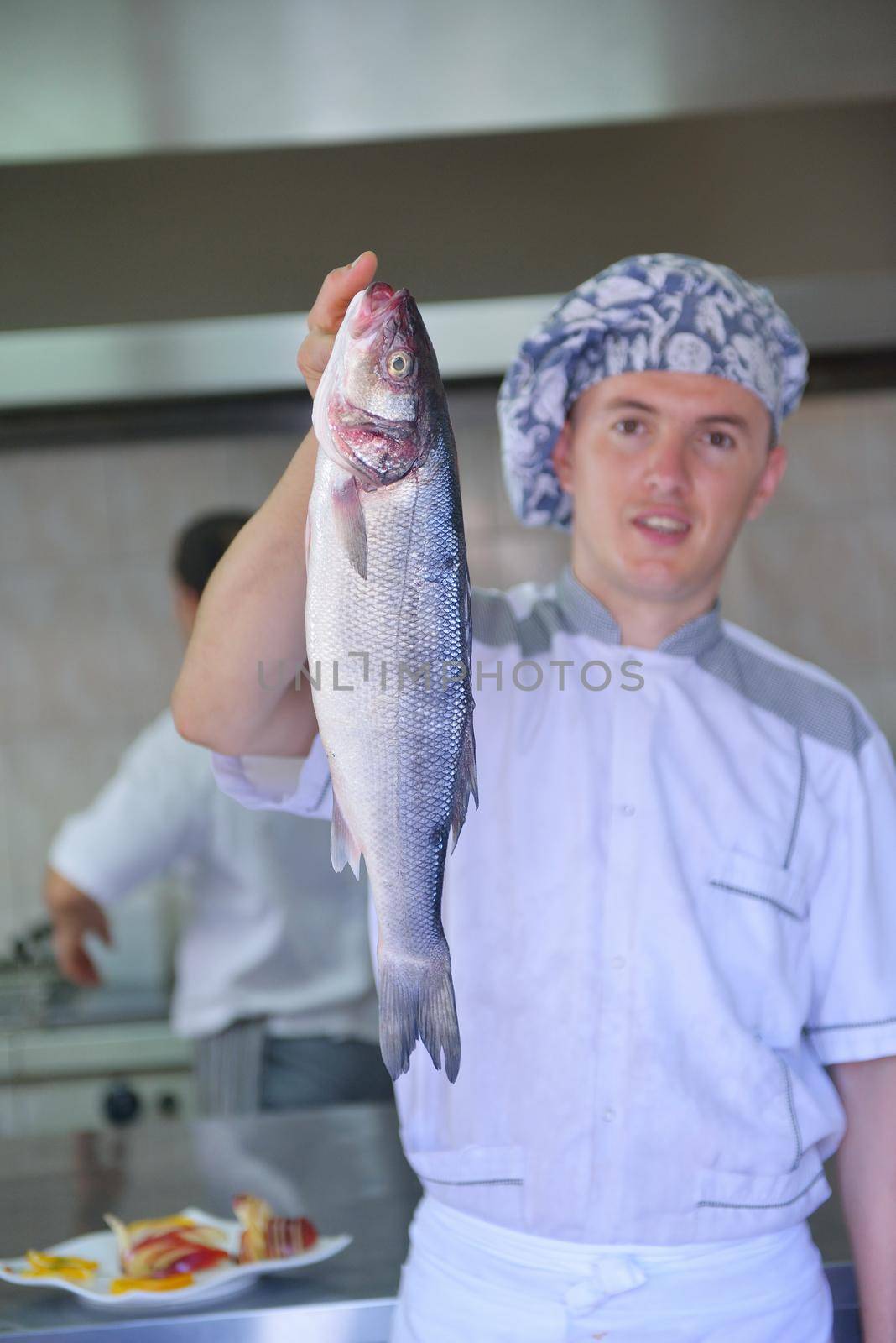 Handsome chef dressed in white uniform decorating pasta salad and seafood fish in modern kitchen