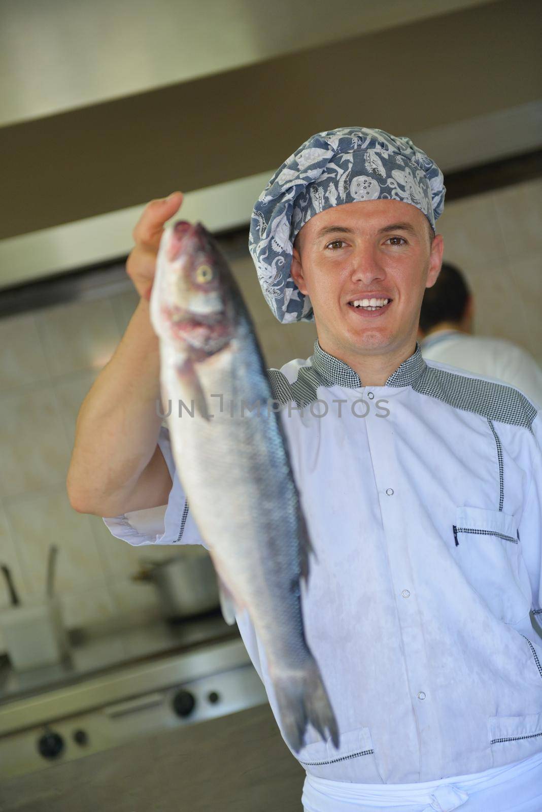 Handsome chef dressed in white uniform decorating pasta salad and seafood fish in modern kitchen