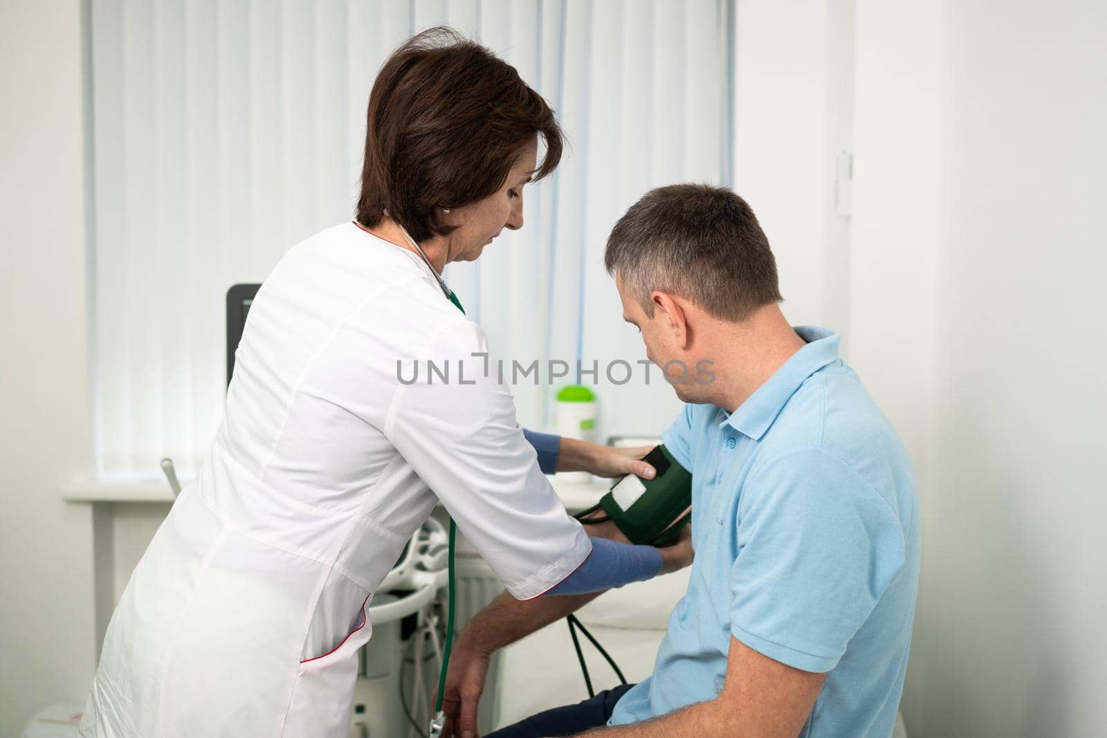 Female doctor measures blood pressure with a sphygmomanometer to male patient at medical examination in clinic office. Cardiologist checks blood pressure of male patient at cardiology hospital.