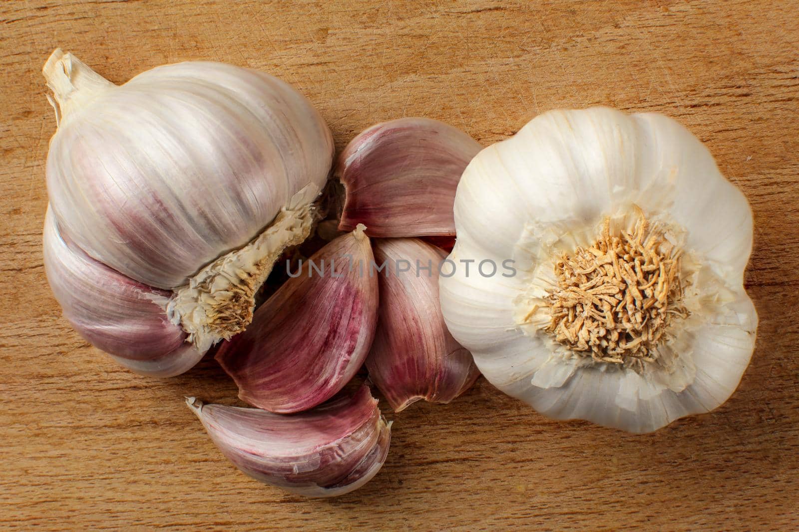 Top view on garlic bulb and cloves placed on old working board with many cuts.