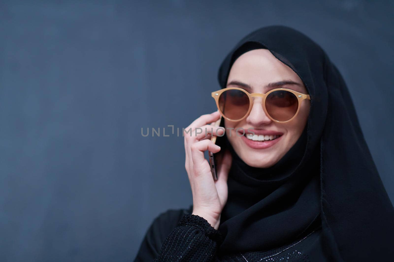 young modern muslim business woman using smartphone wearing sunglasses and hijab clothes in front of black chalkboard