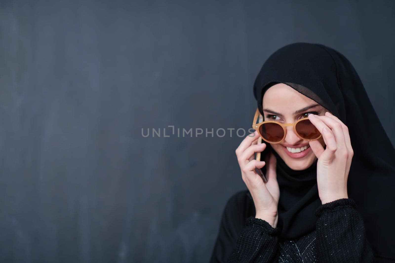 young muslim woman wearing sunglasses using smartphone by dotshock