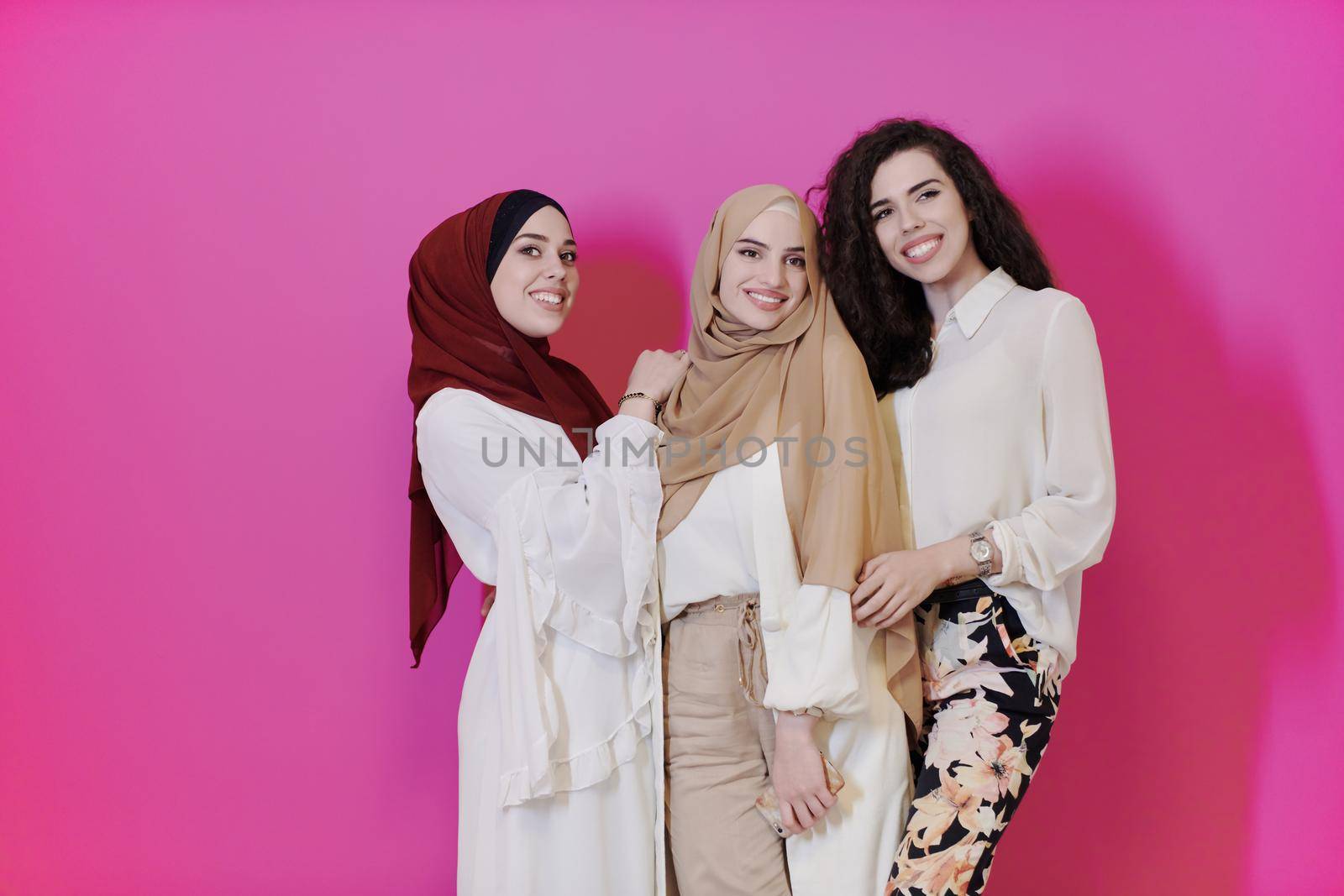 group portrait of beautiful muslim women two of them in fashionable dress with hijab isolated on pink background representing modern islam fashion and ramadan kareem concept