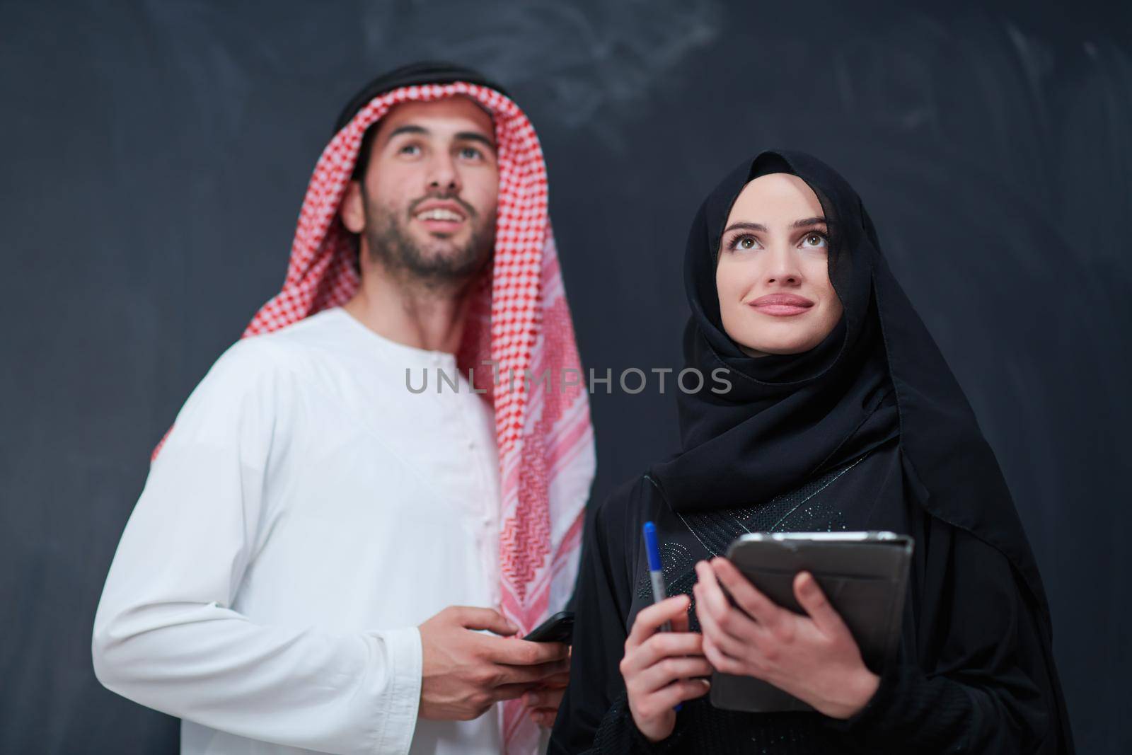 muslim couple using modern technology in front of black chalkboard by dotshock