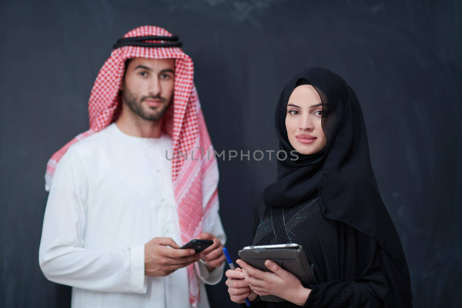 muslim couple using modern technology in front of black chalkboard by dotshock