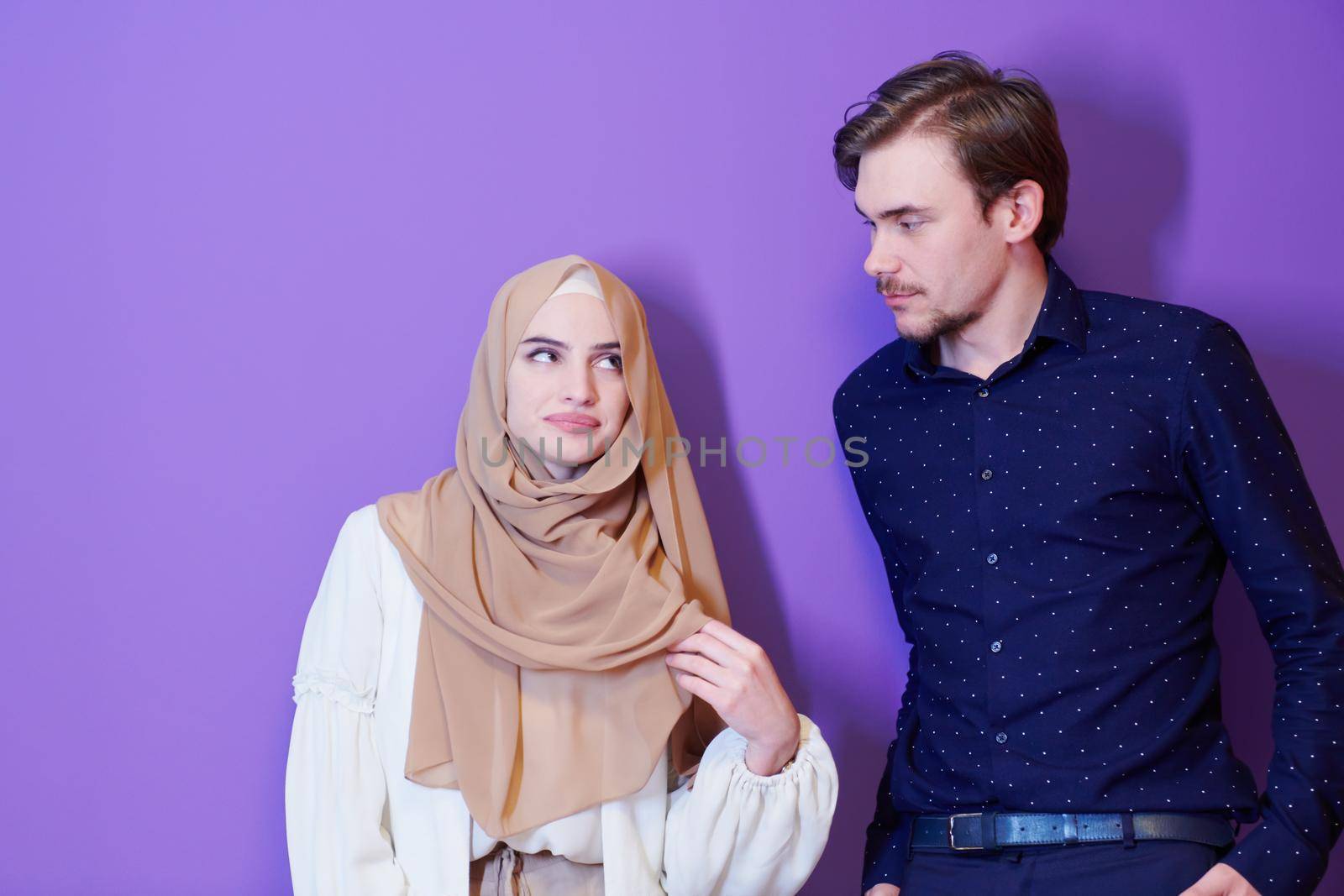 portrait of young muslim couple woman in fashionable dress with hijab isolated on purple background representing modern islam fashion and ramadan kareem concept