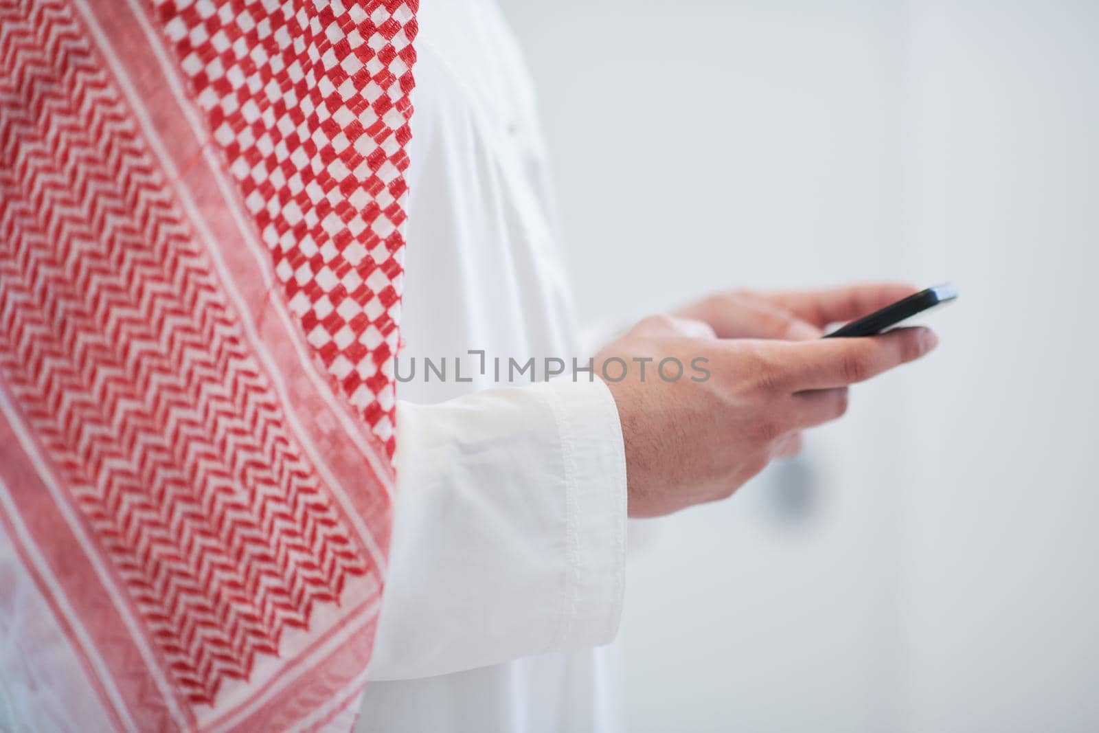 young modern muslim arabian businessman wearing traditional clothes while using smartphone at home