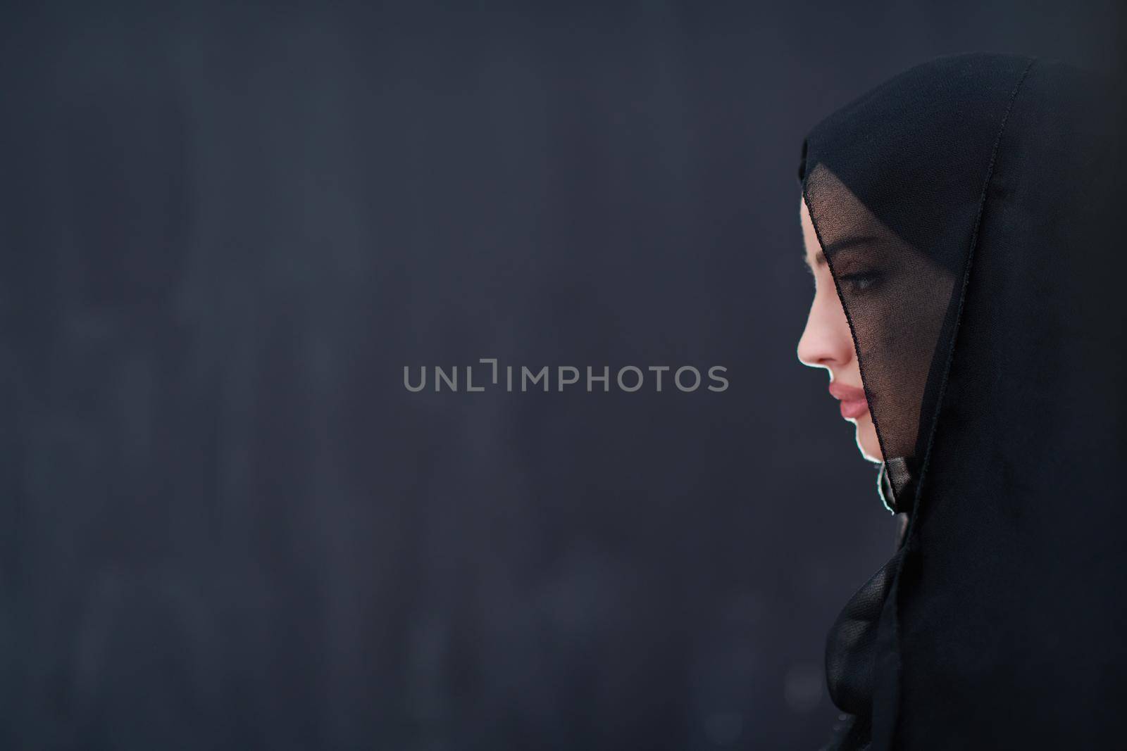 portrait of beautiful muslim woman in fashionable dress with hijab in front of black chalkboard representing modern islam fashion and ramadan kareem concept