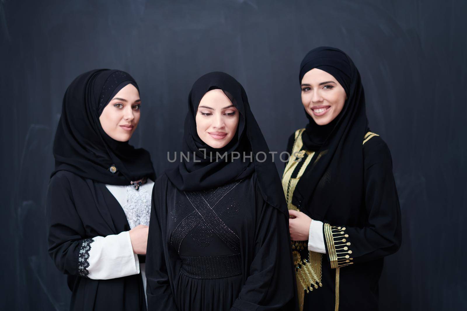 group portrait of beautiful muslim women in fashionable dress with hijab isolated on black chalkboard background representing modern islam fashion and ramadan kareem concept