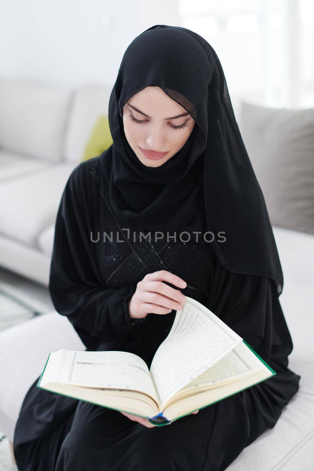 young muslim woman reading Quran at home by dotshock