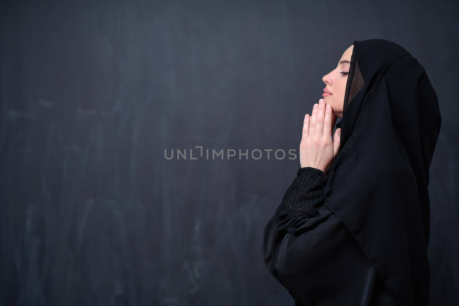 muslim woman making traditional prayer to God in front of black chalkboard by dotshock