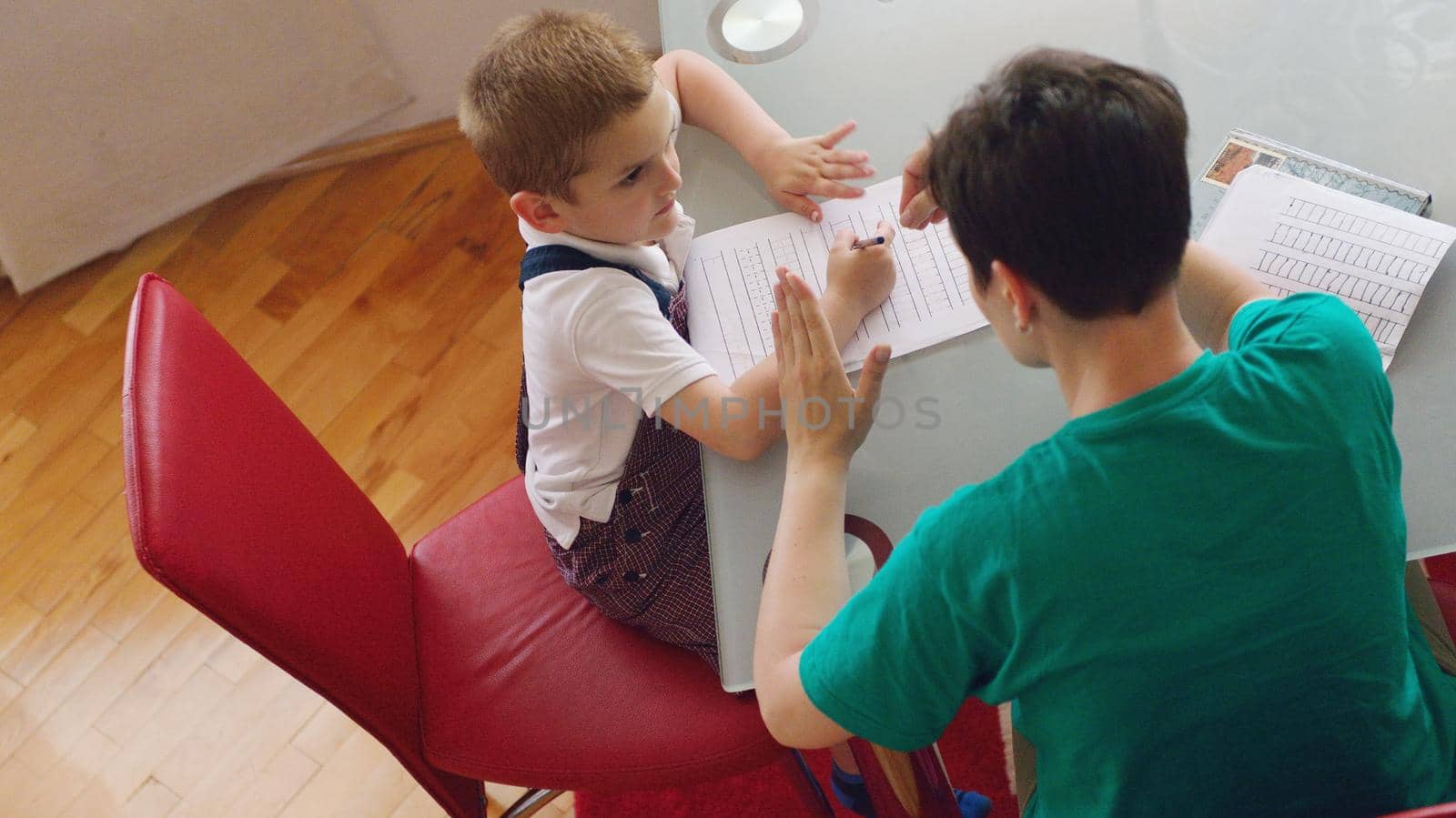 young mom woman doing home work with elementary school grade boy at home in kitchen