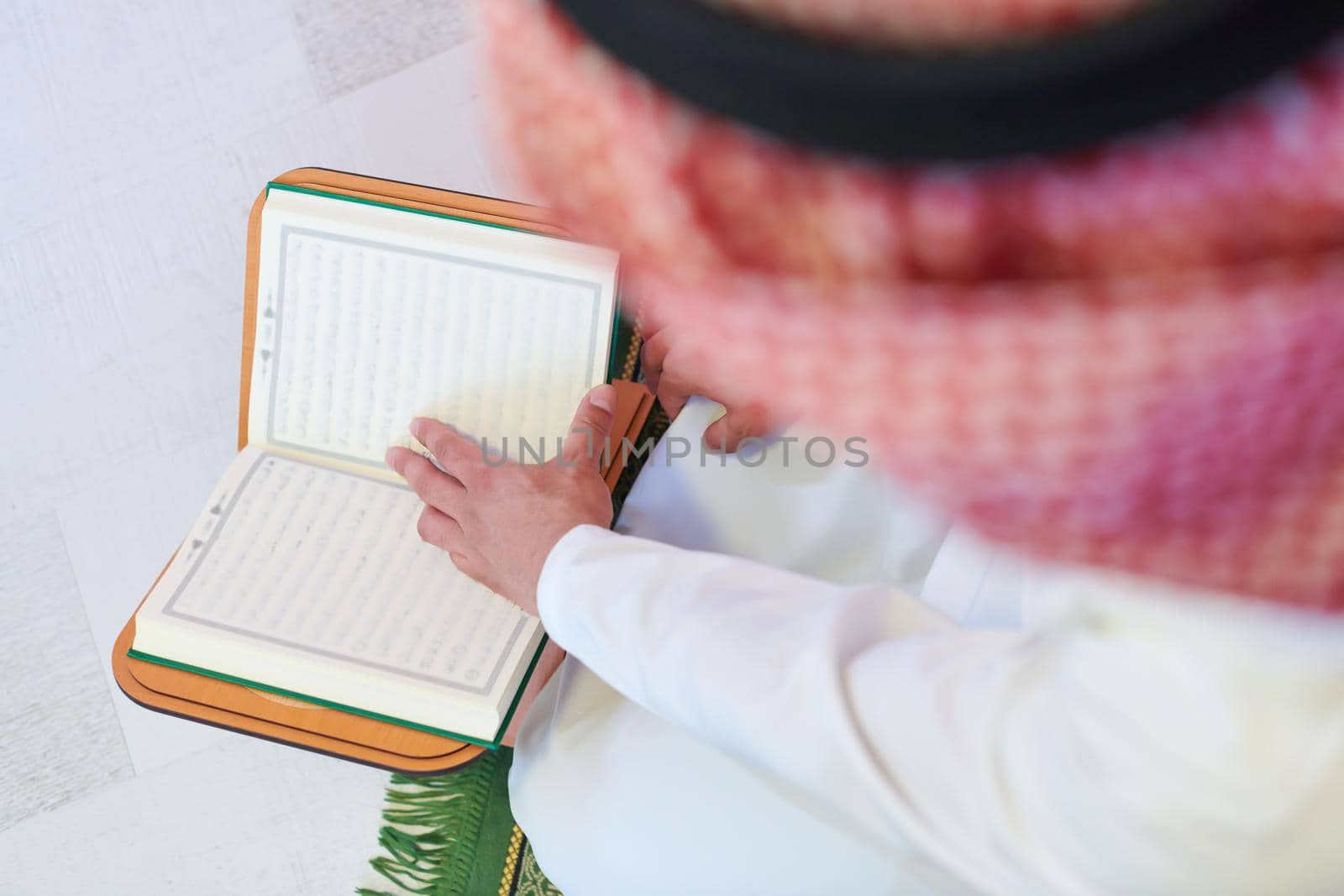 young arabian muslim man in traditional clothes reading holy book Quran on the praying carpet before iftar dinner during a ramadan feast at home