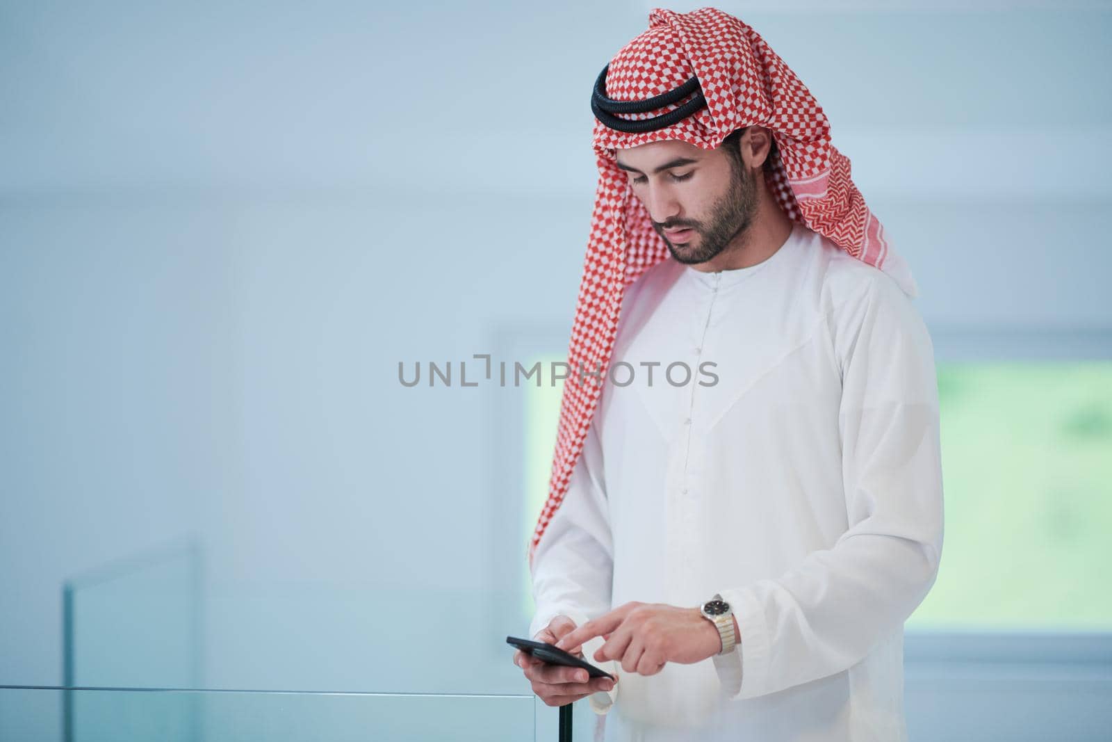 young modern muslim arabian businessman wearing traditional clothes while using smartphone at home