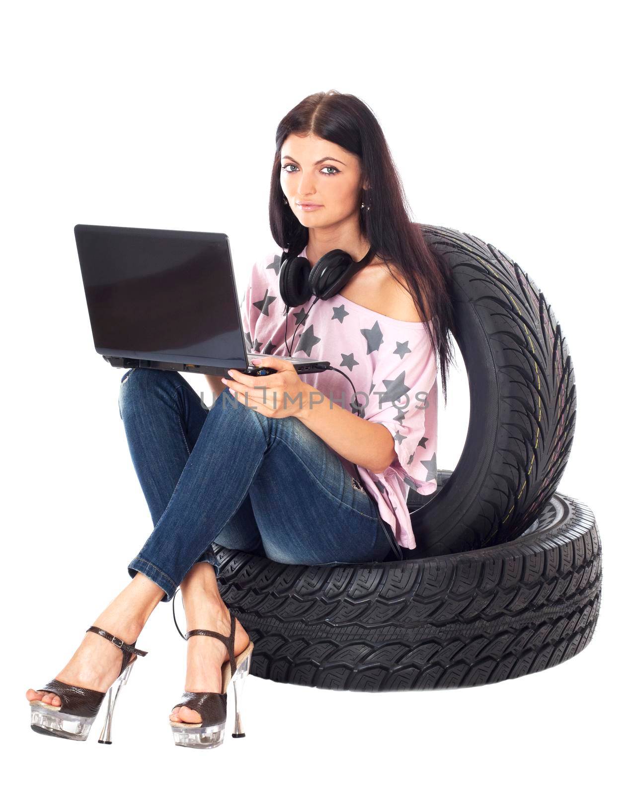 Young sexy woman with laptop and headset sitting on the car wheels, isolated on white.