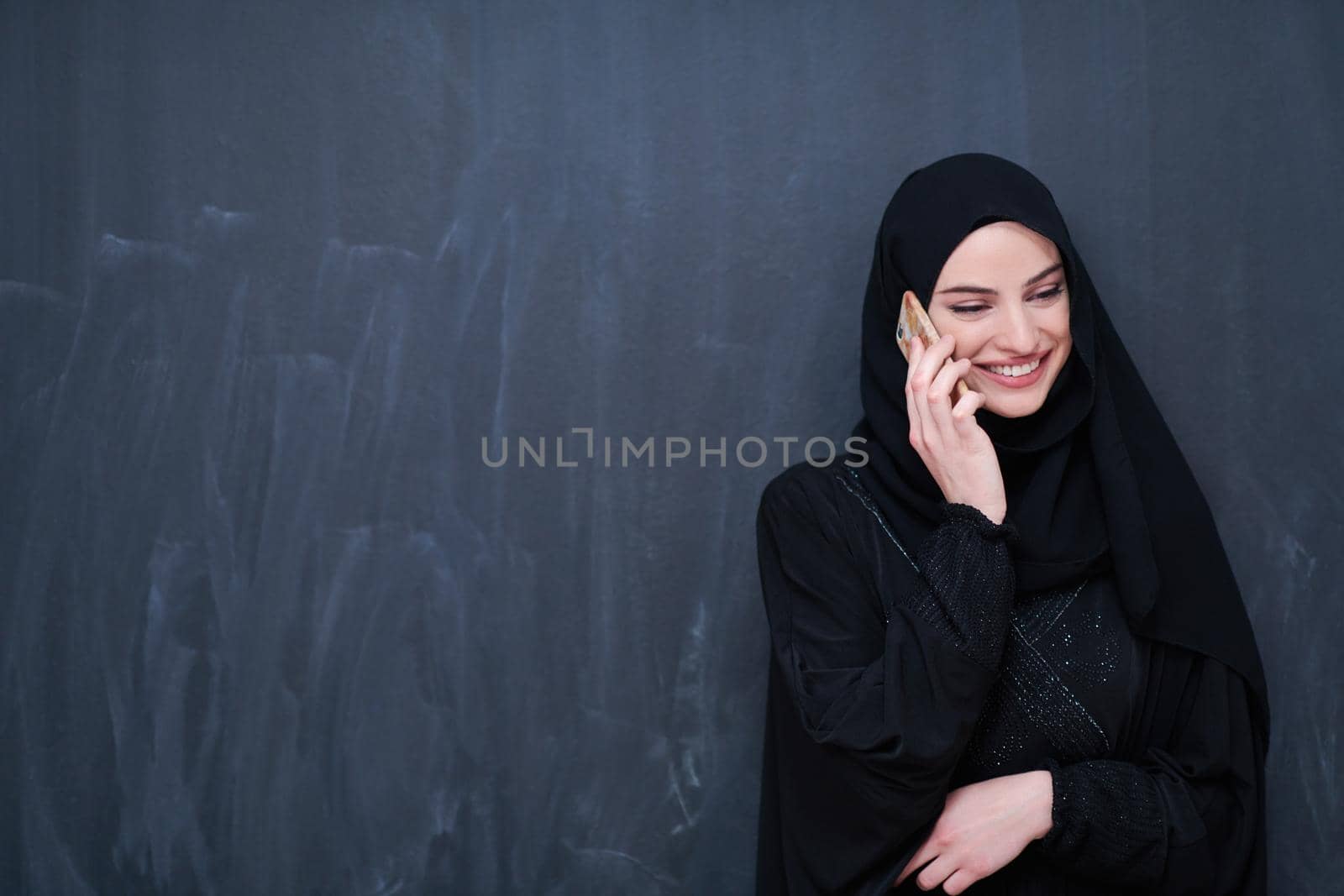 young modern muslim business woman using smartphone wearing hijab clothes in front of black chalkboard