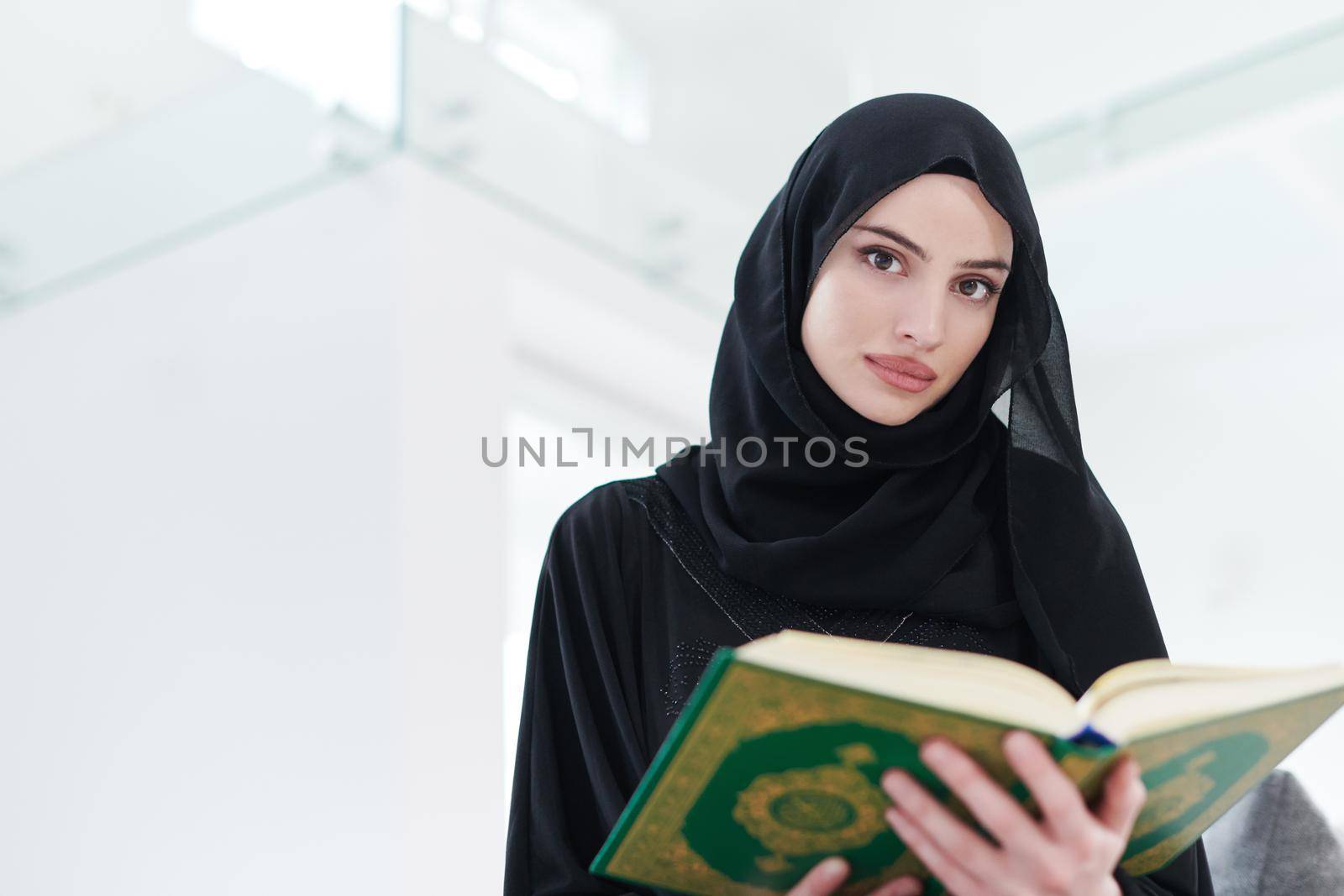 young traditional muslim woman reading Quran on the sofa before iftar dinner during a ramadan feast at home