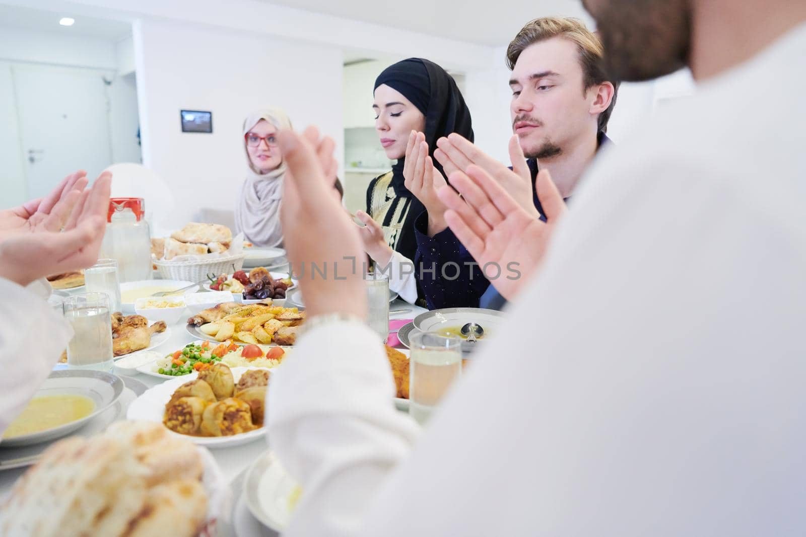 Eid Mubarak Muslim people praying before iftar dinner. Eating traditional food during Ramadan feasting month at home. The Islamic Halal Eating and Drinking at modern western Islamic family