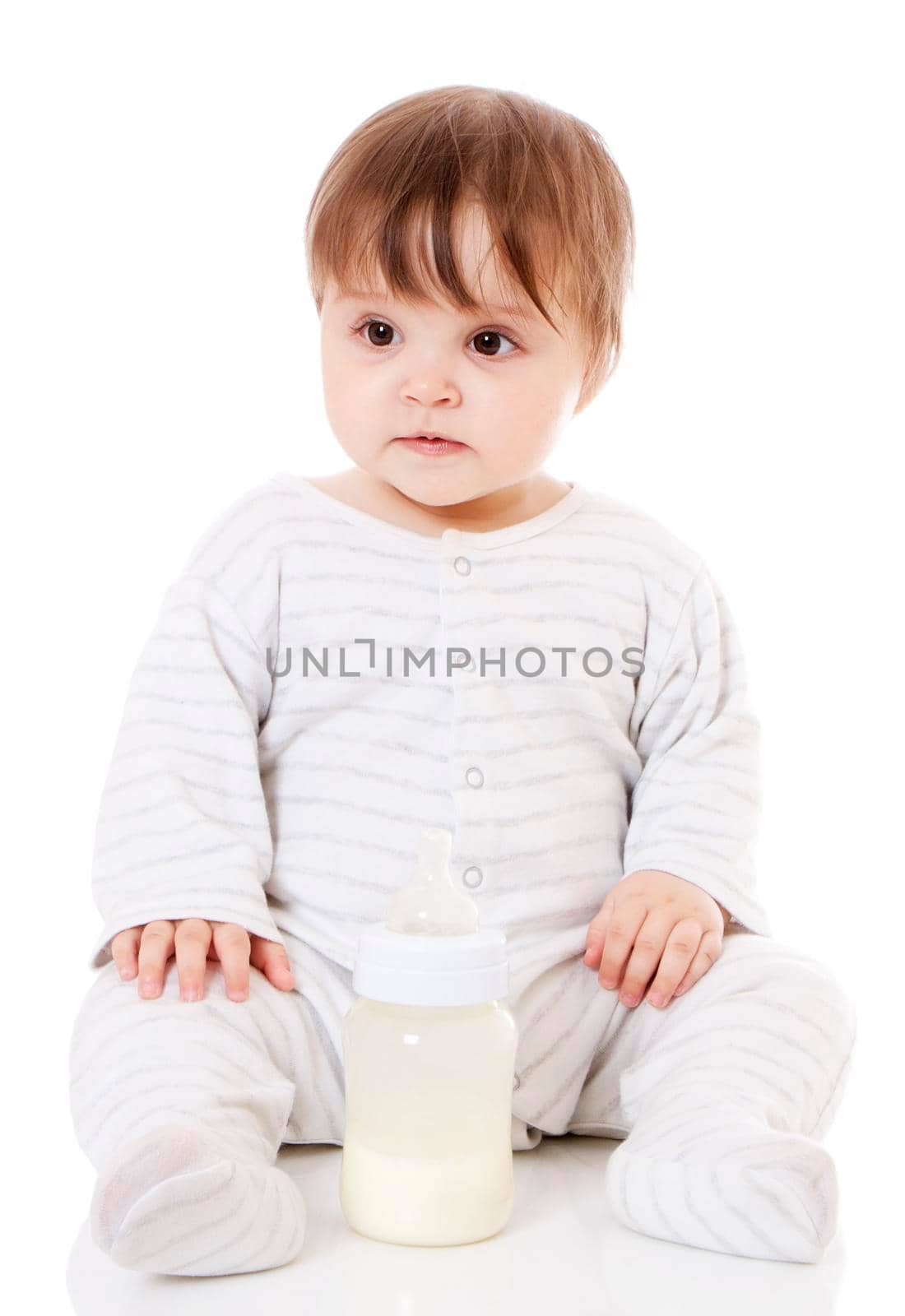 Newborn baby sitting on the floor with the bottle. Isolsted on white.