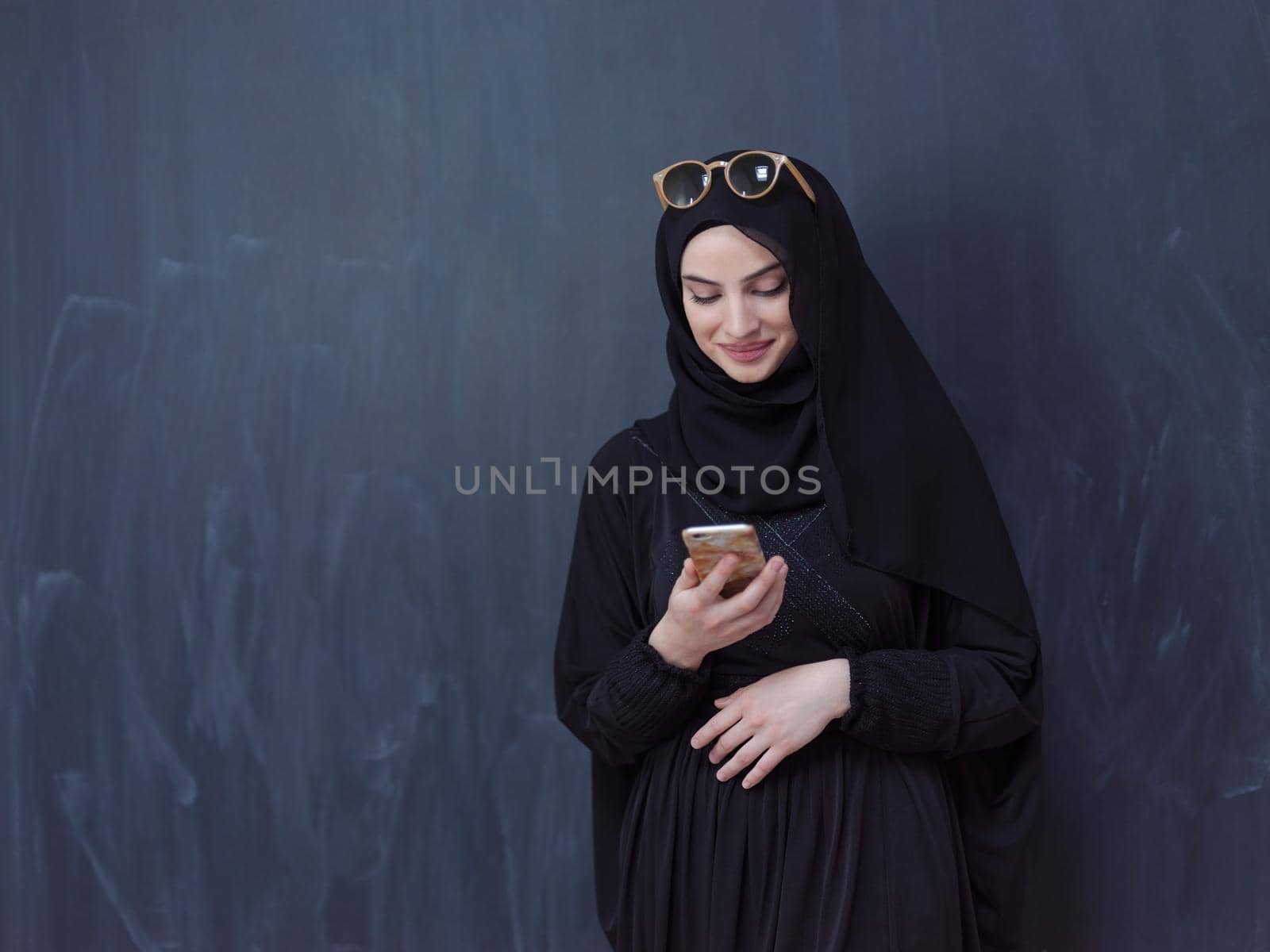 young muslim woman wearing sunglasses using smartphone by dotshock