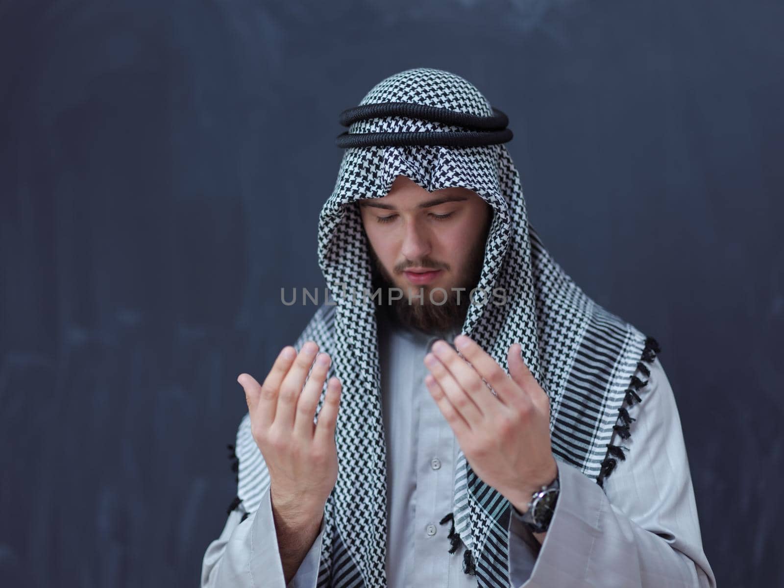 arabian man making traditional prayer to God, keeps hands in praying gesture in front of black chalkboard by dotshock