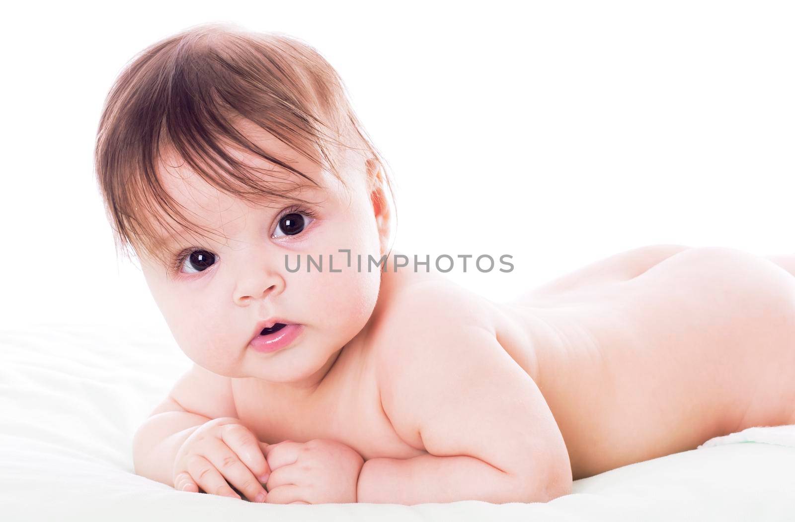 Cute baby lying on stomach on white floor background and smiling big.