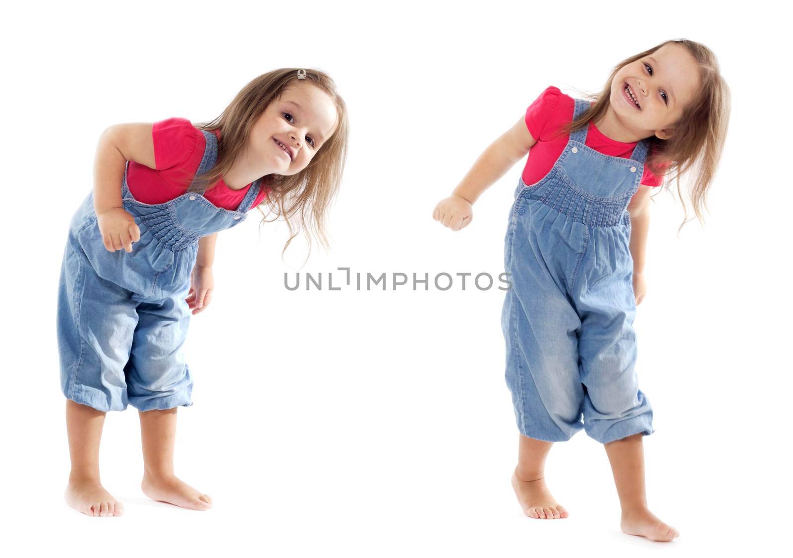 Happy toddler girl wearing jeans jumpsuit is having a great time dancing in the studio. Isolated on white.