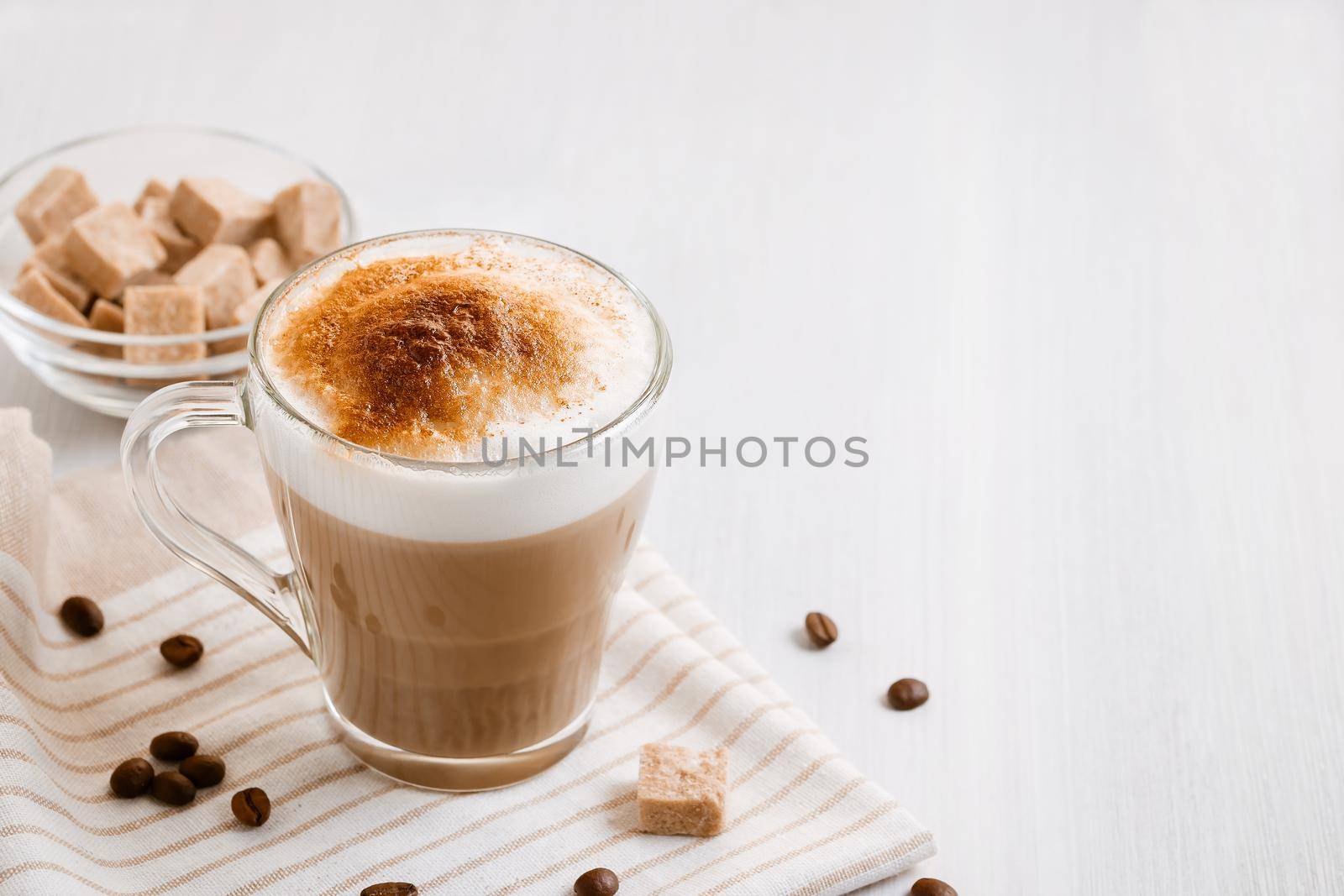 Latte coffee poured in layers with froth and a crispy chocolate top on a light kitchen table.