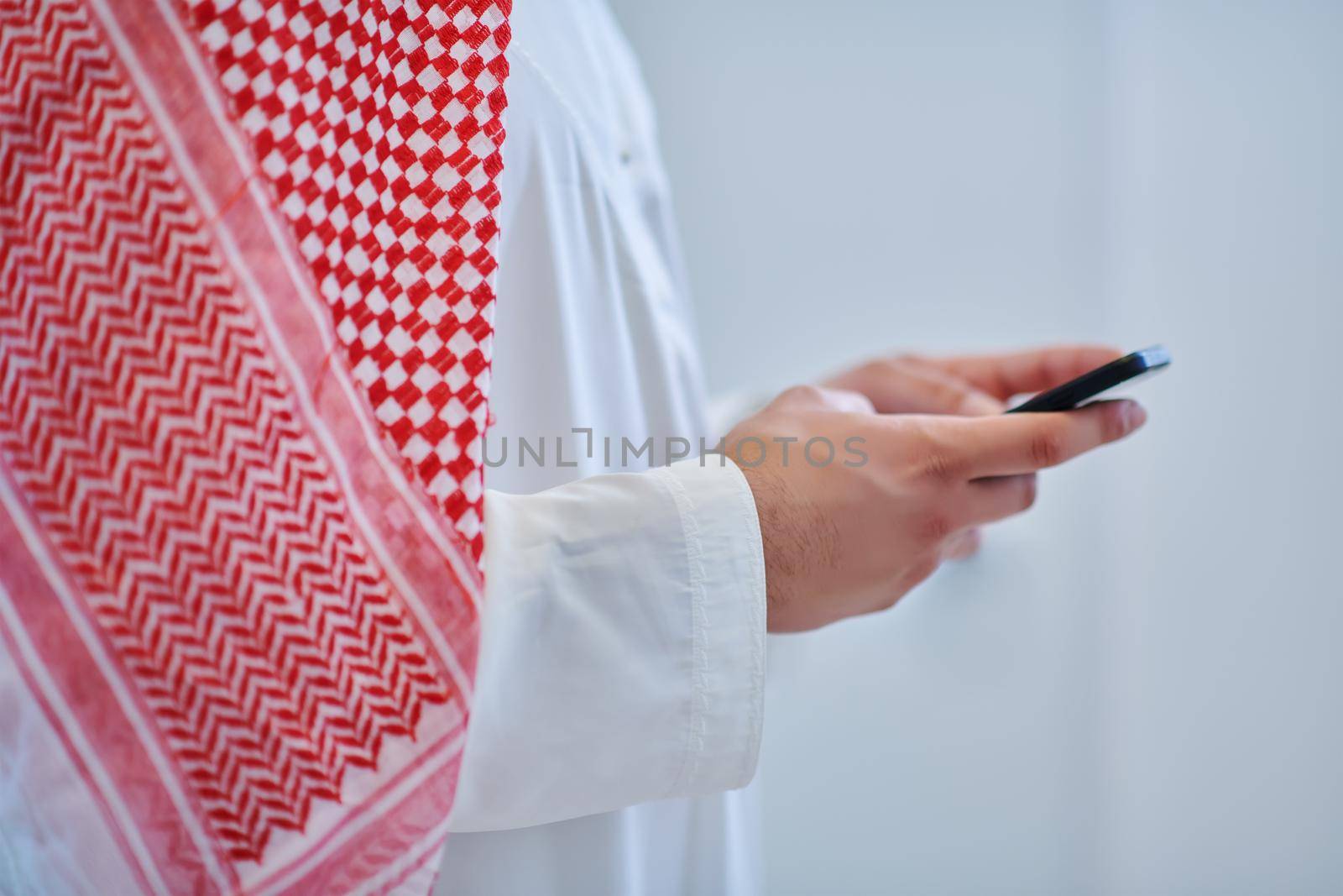 Portrait of young muslim businessman using mobile phone. Successful Arab boy in traditional clothes representing technology